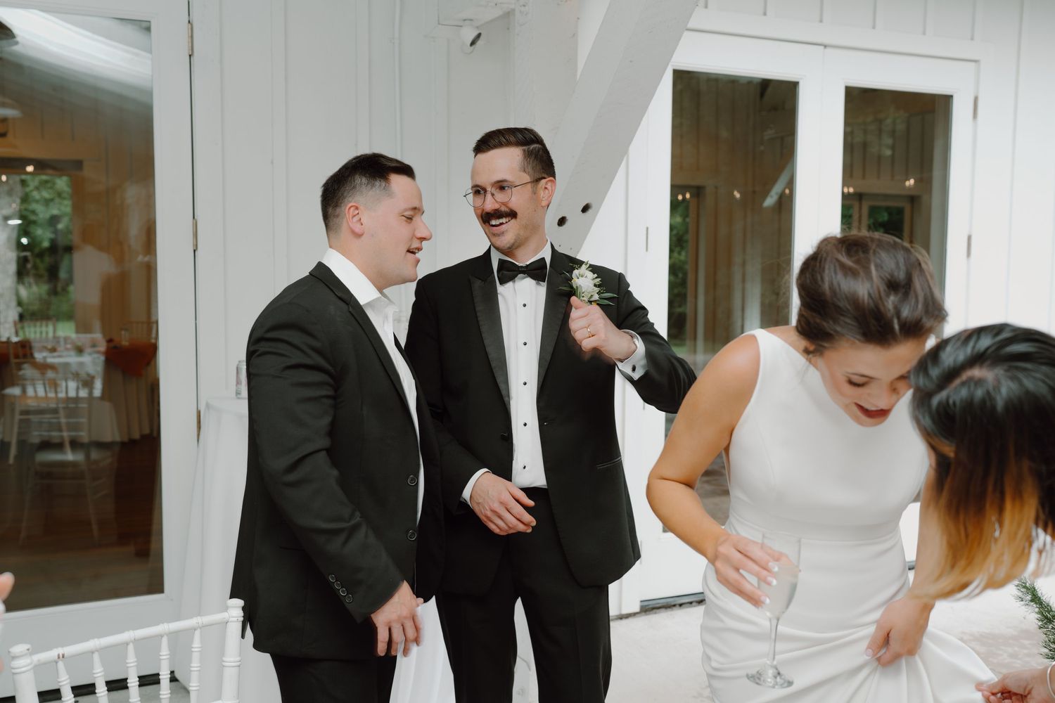 Wedding party members sharing joyful moments in a white-walled venue.