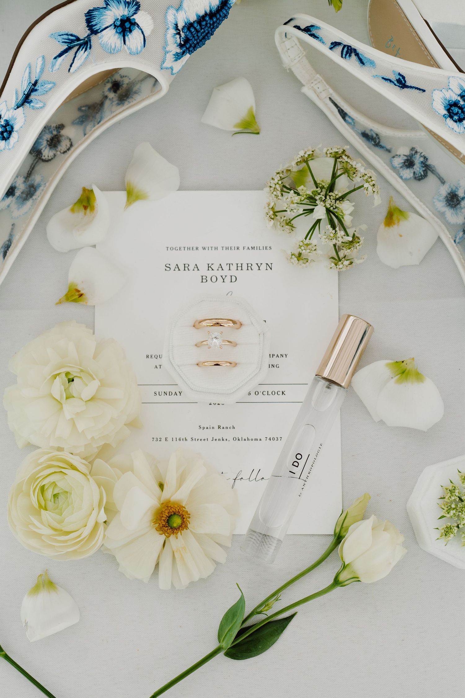 Wedding stationery and blue marbled details arranged with white flowers and rings.