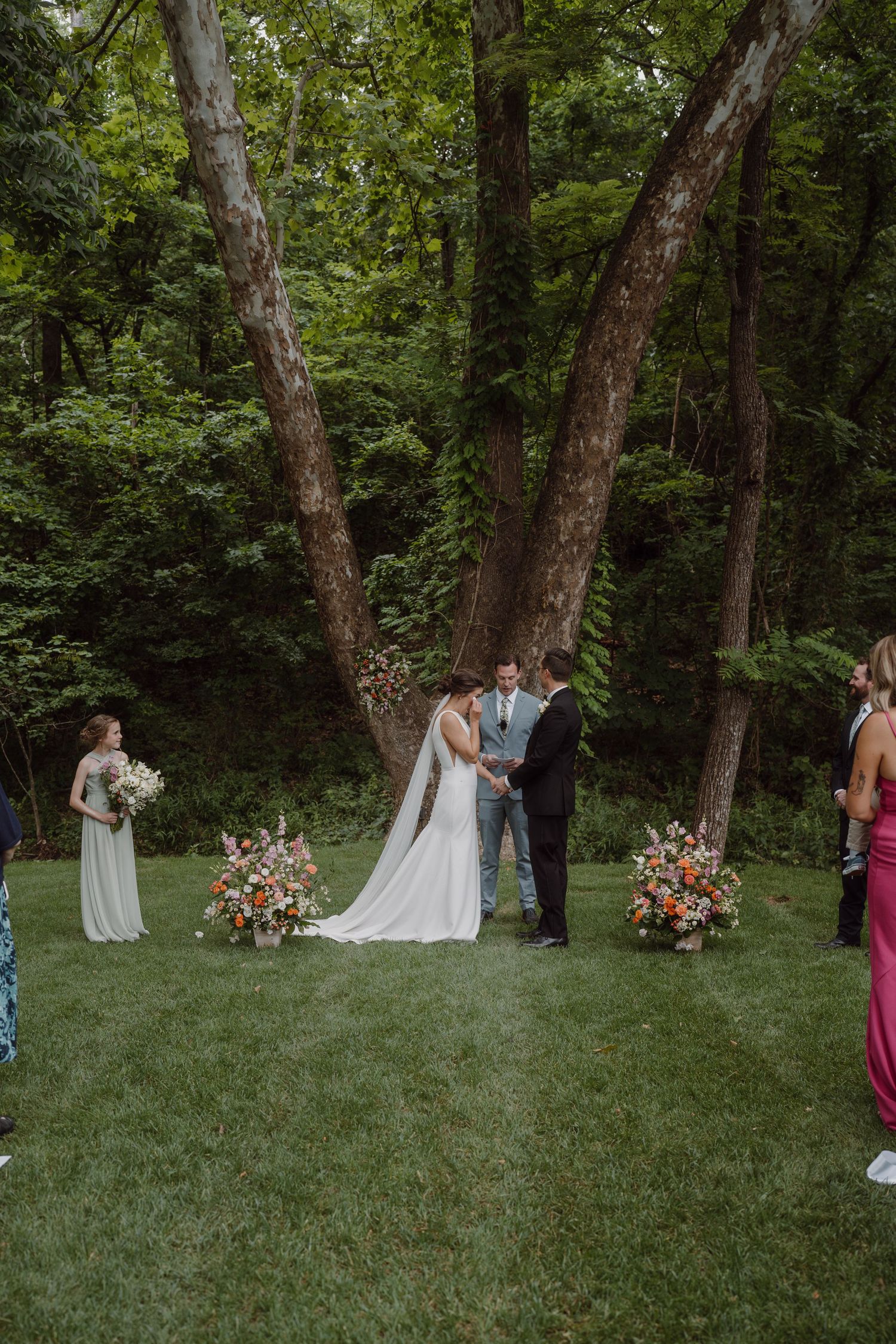 Wedding ceremony setup in a forest clearing with floral arrangements and guests.