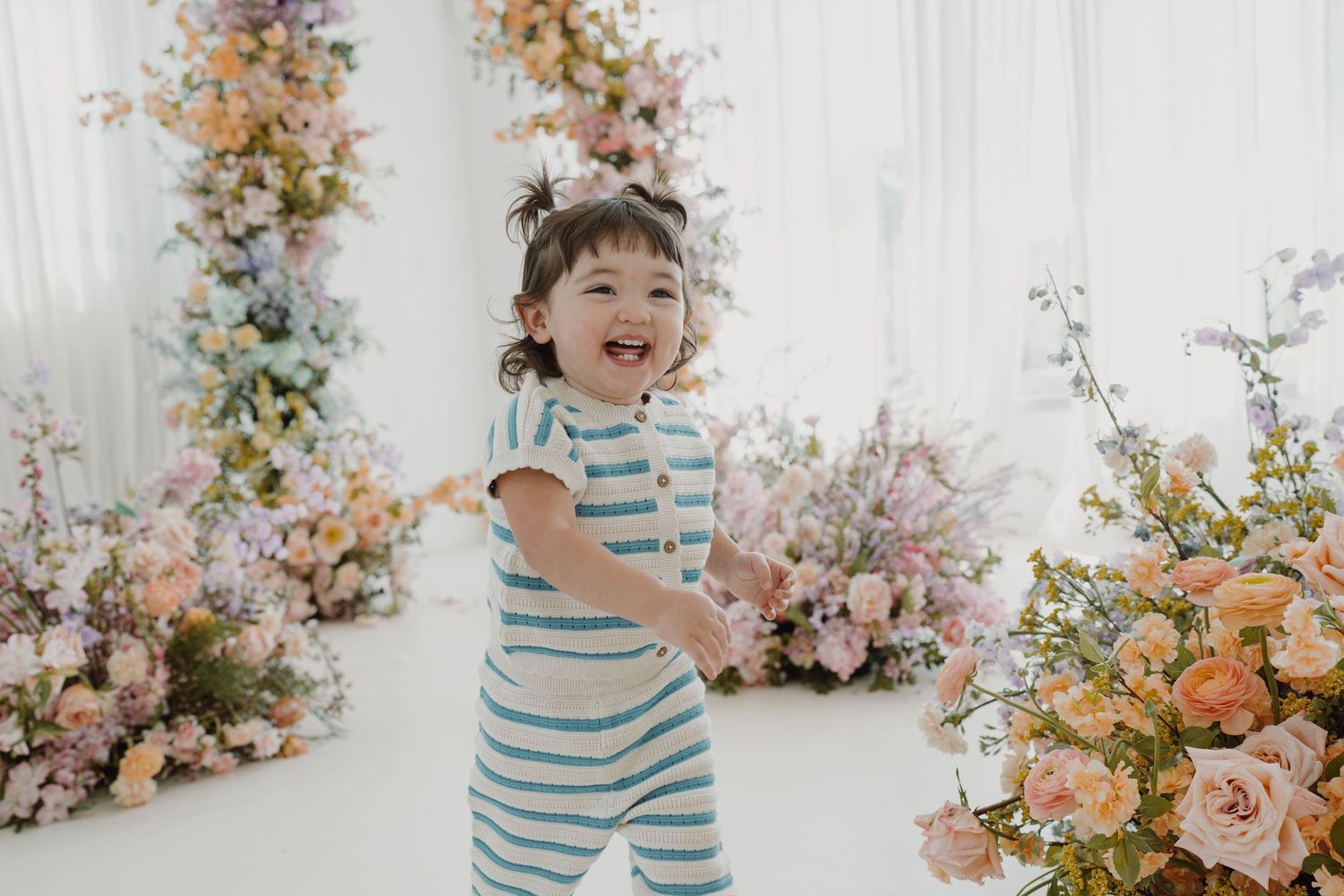 Candid moment of laughing toddler in striped outfit with floral backdrop.