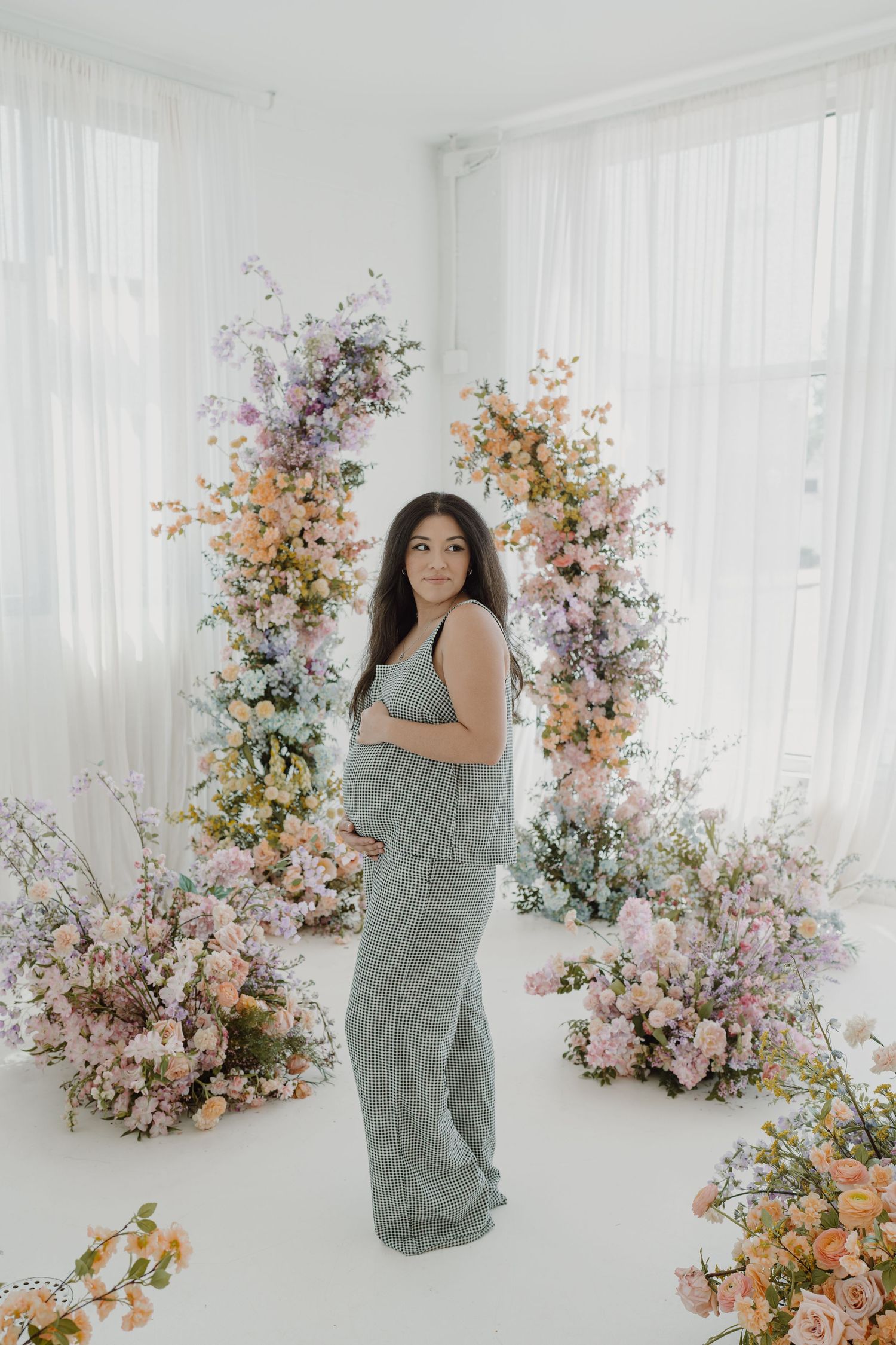 Artistic maternity photography in a white studio surrounded by blooming spring flowers.