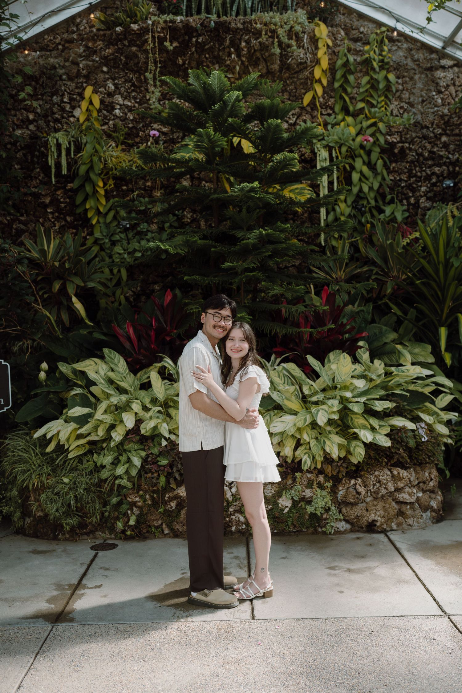 Couple sharing a romantic moment on a garden path with lush tropical plants in the background.
