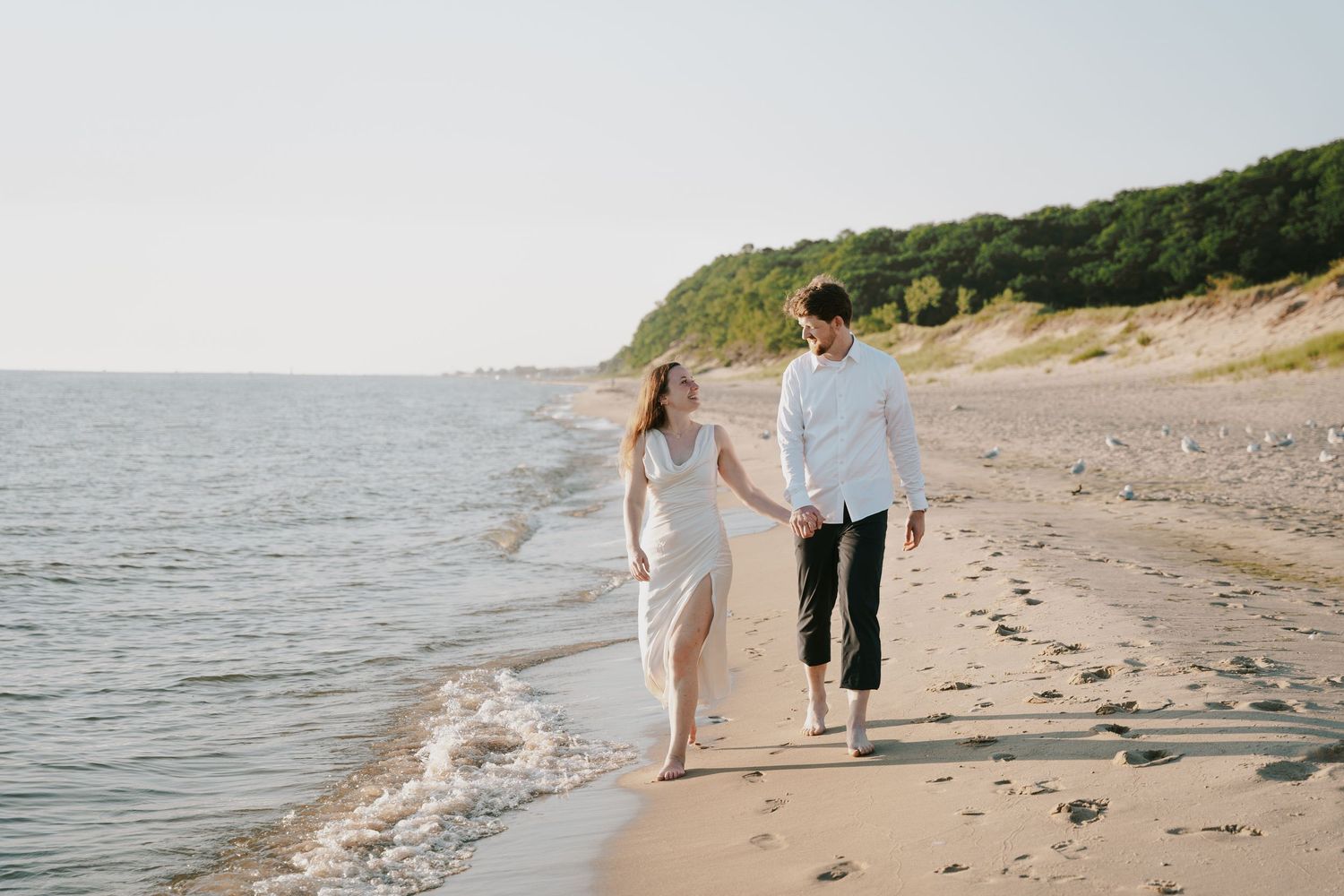 Couple taking a romantic stroll along a scenic beach with cliffs in the background.