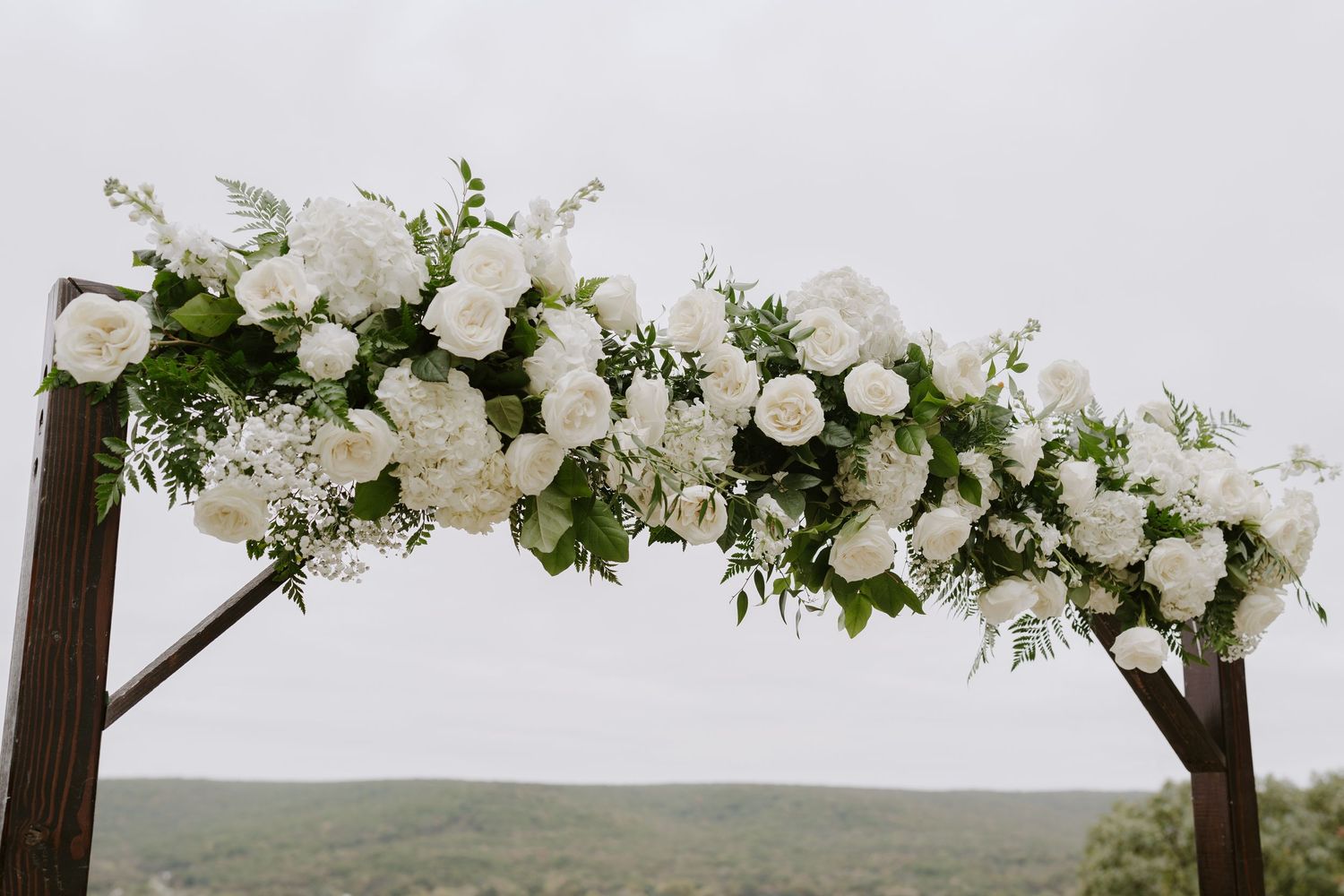 White floral arch arrangement decorates the top of a wooden wedding ceremony structure.