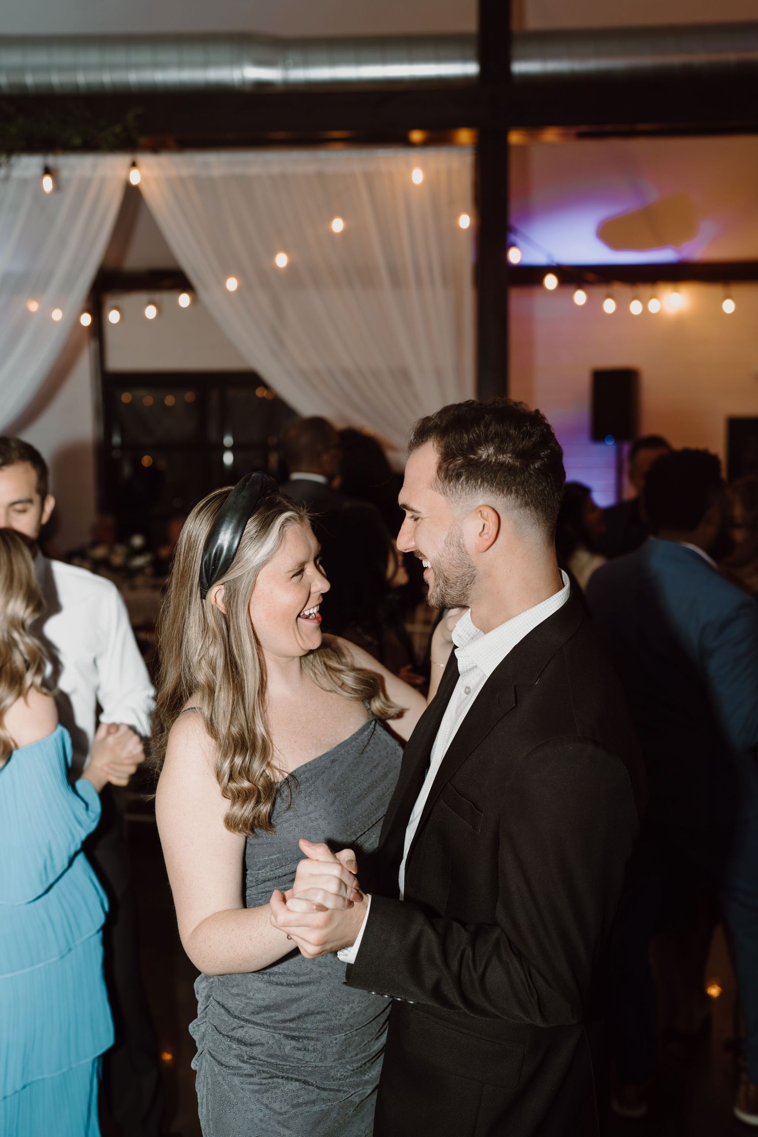 Couples dancing together under string lights at an evening wedding reception.