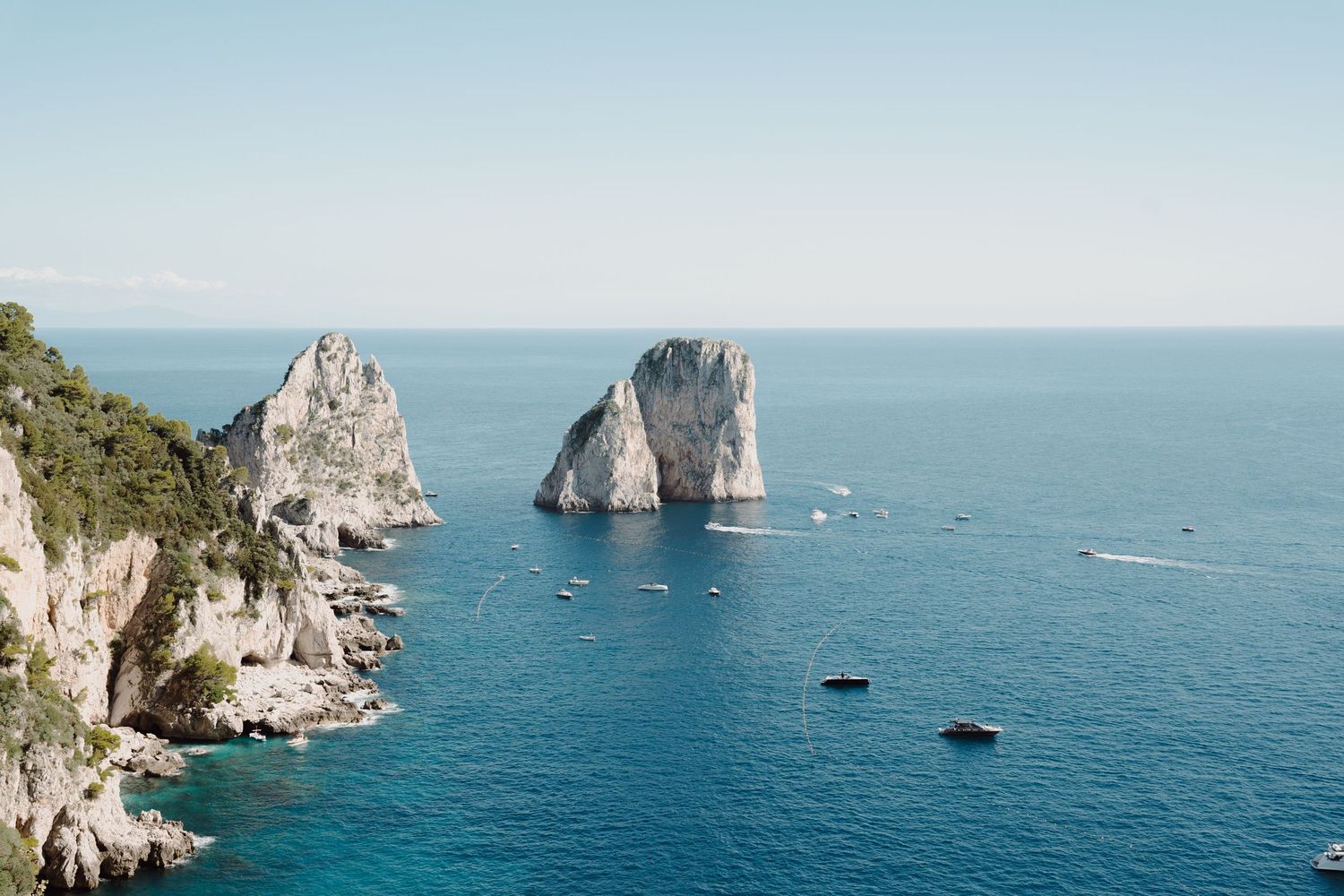 Crystal blue Mediterranean waters surrounding the iconic Faraglioni rocks off the coast of Capri.