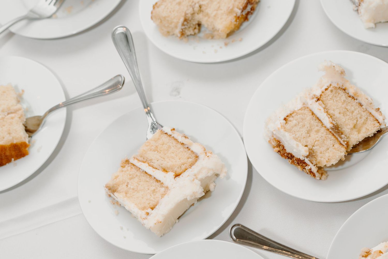 Slices of wedding cake plated on white dishes with forks at a reception.