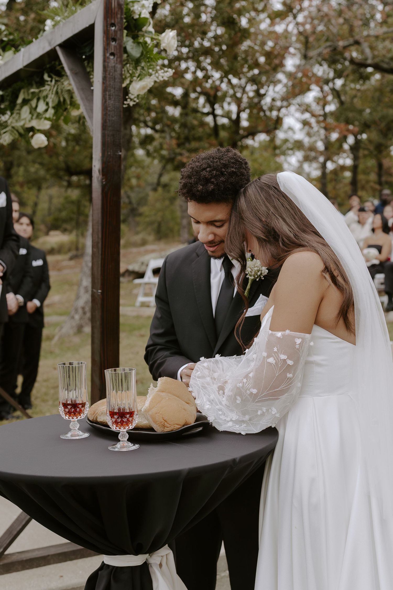 Wedding couple signing documents at outdoor ceremony table with wine glasses.