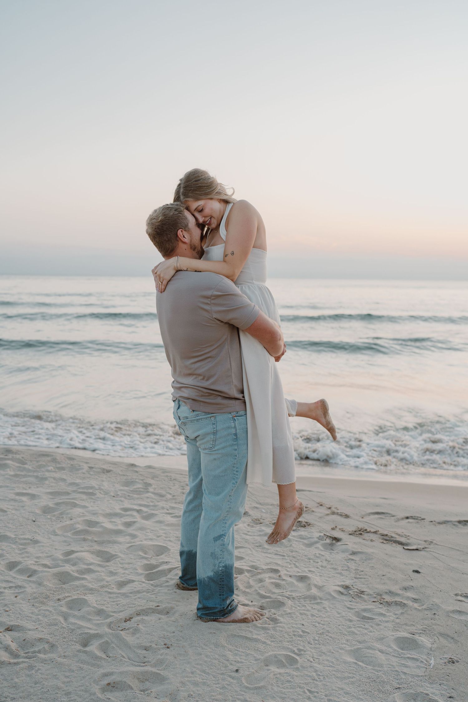 A couple shares a romantic moment on the beach with ocean waves and sunset in the background.