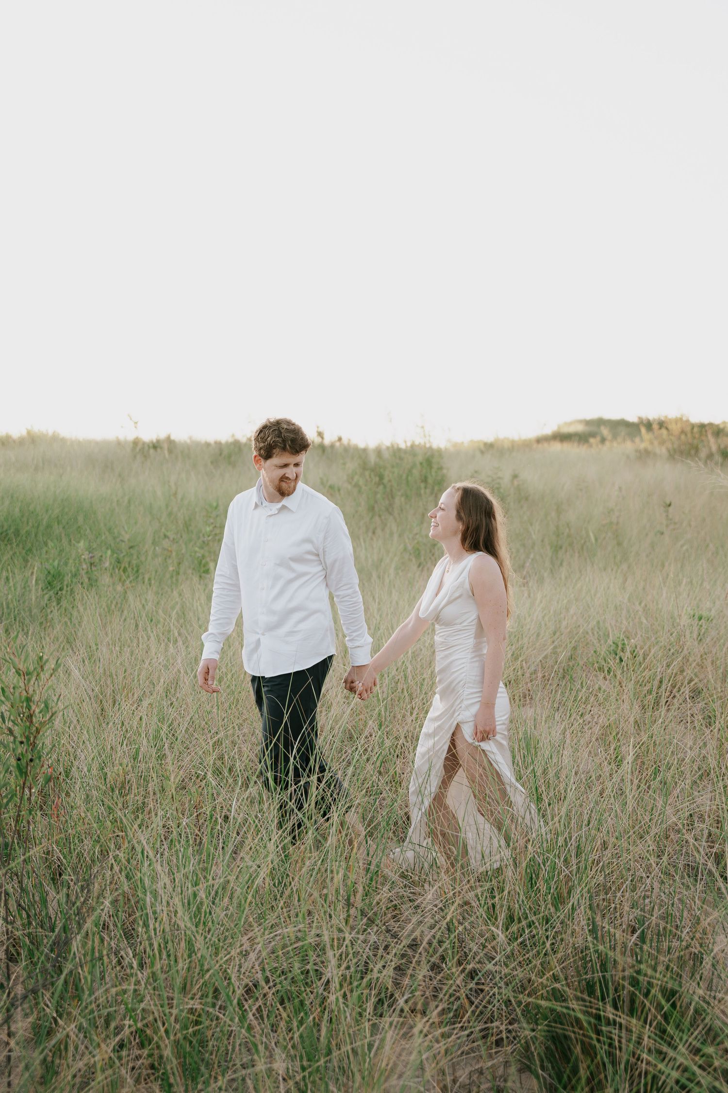 Two people walk through wild grass in a natural meadow setting.