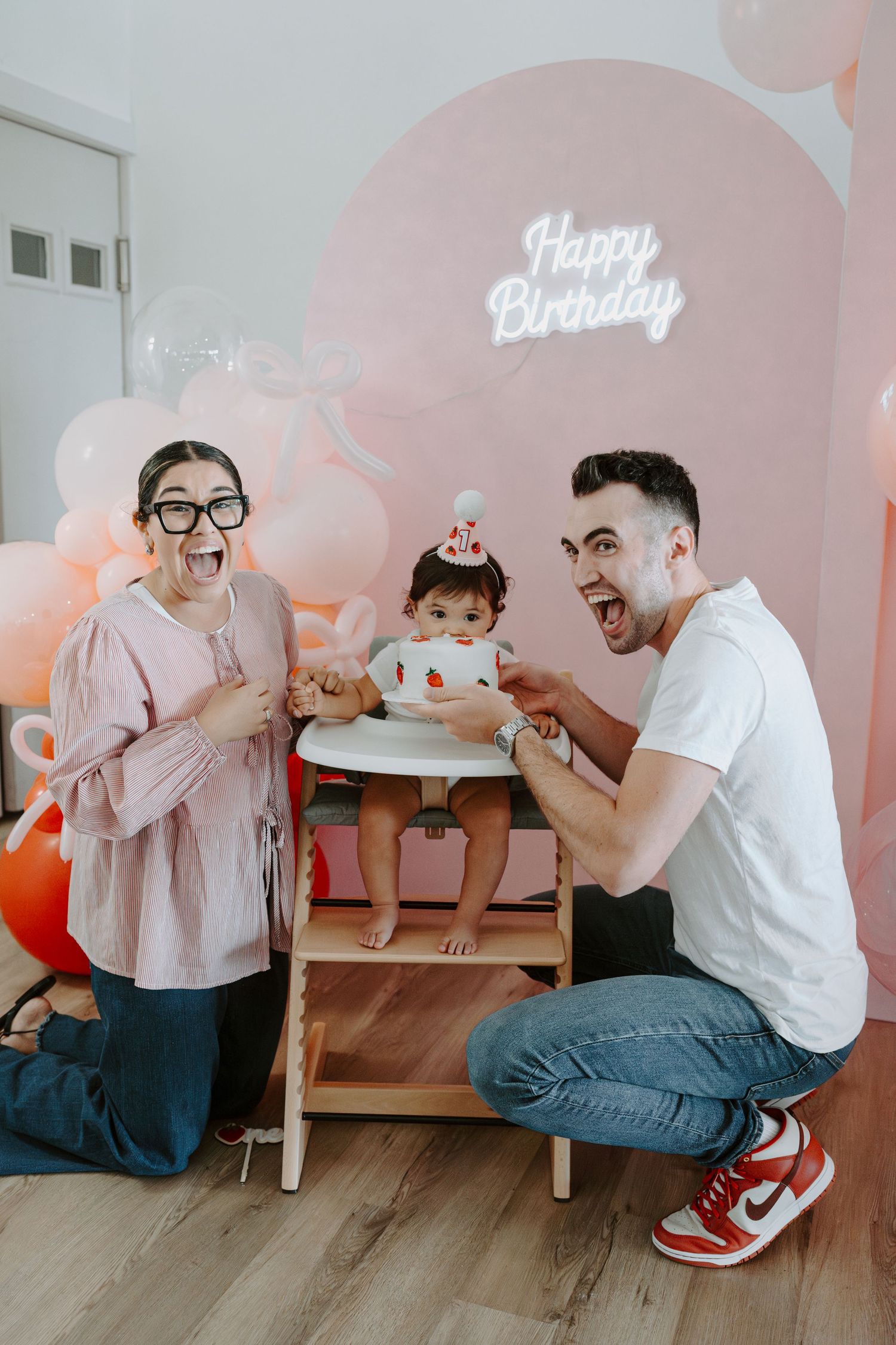 Energetic family moment during baby's birthday party with pink decorations and neon sign.