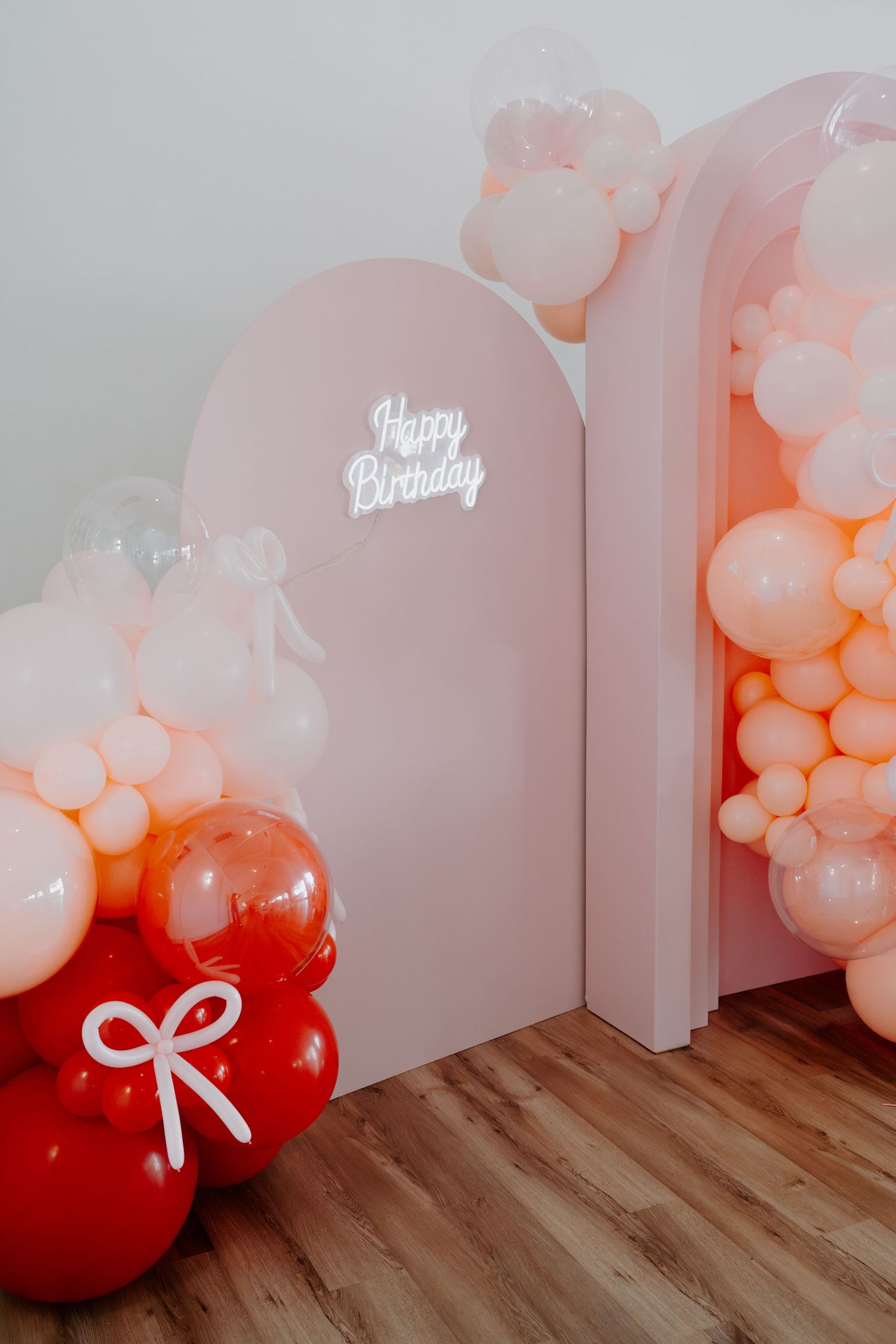 Decorative balloon garland in pink and red with 'Happy Birthday' sign on wall.