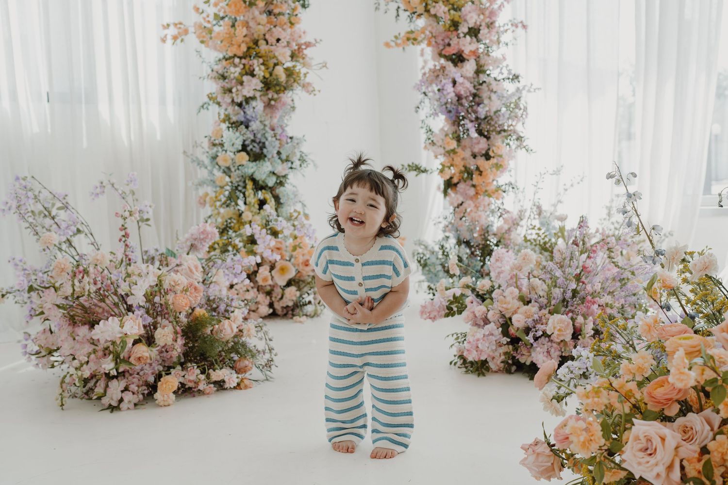 Dreamy photography setup with pastel floral arrangements against white drapes.