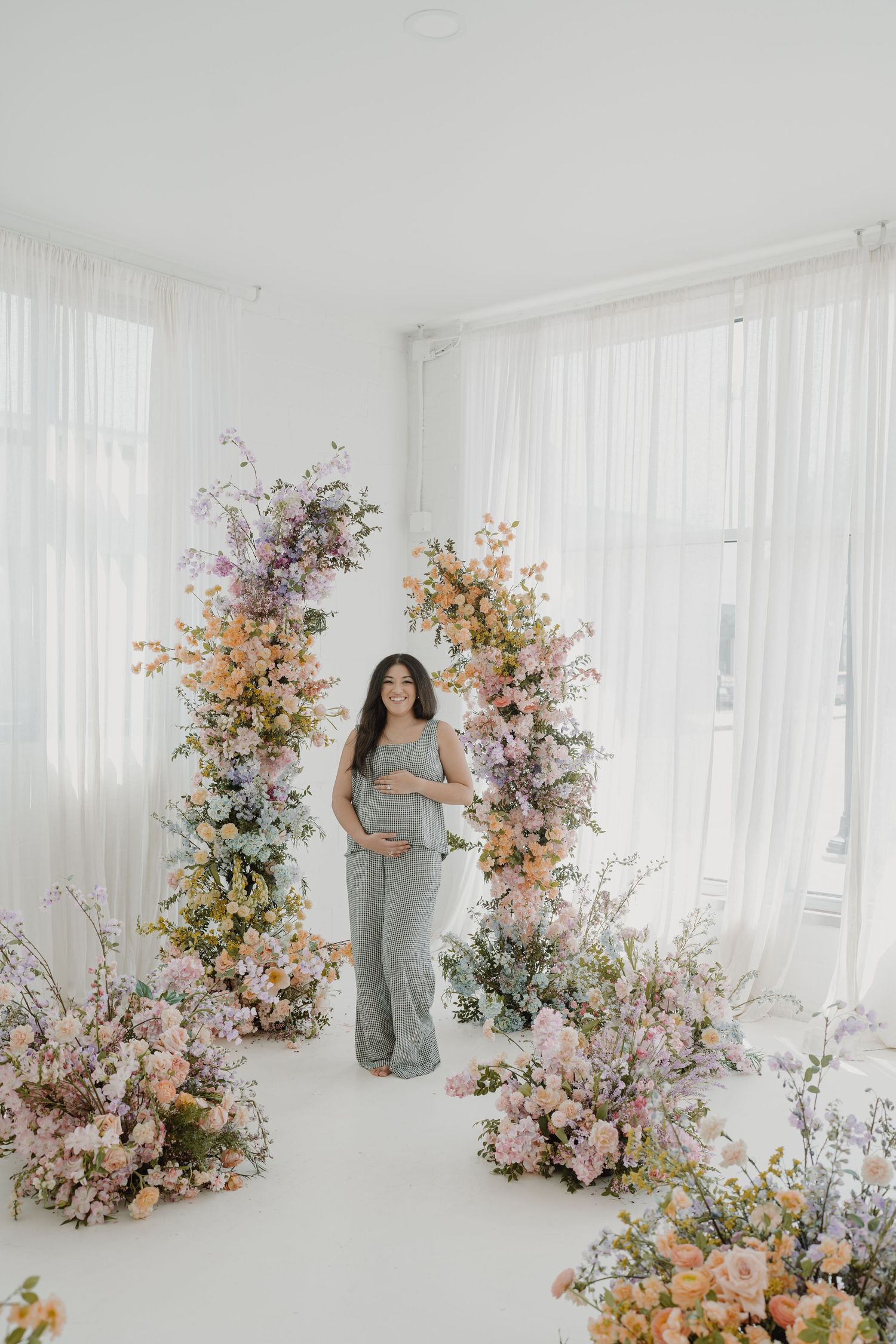 Maternity photoshoot in bright white studio with beautiful floral arrangements in pastel colors.