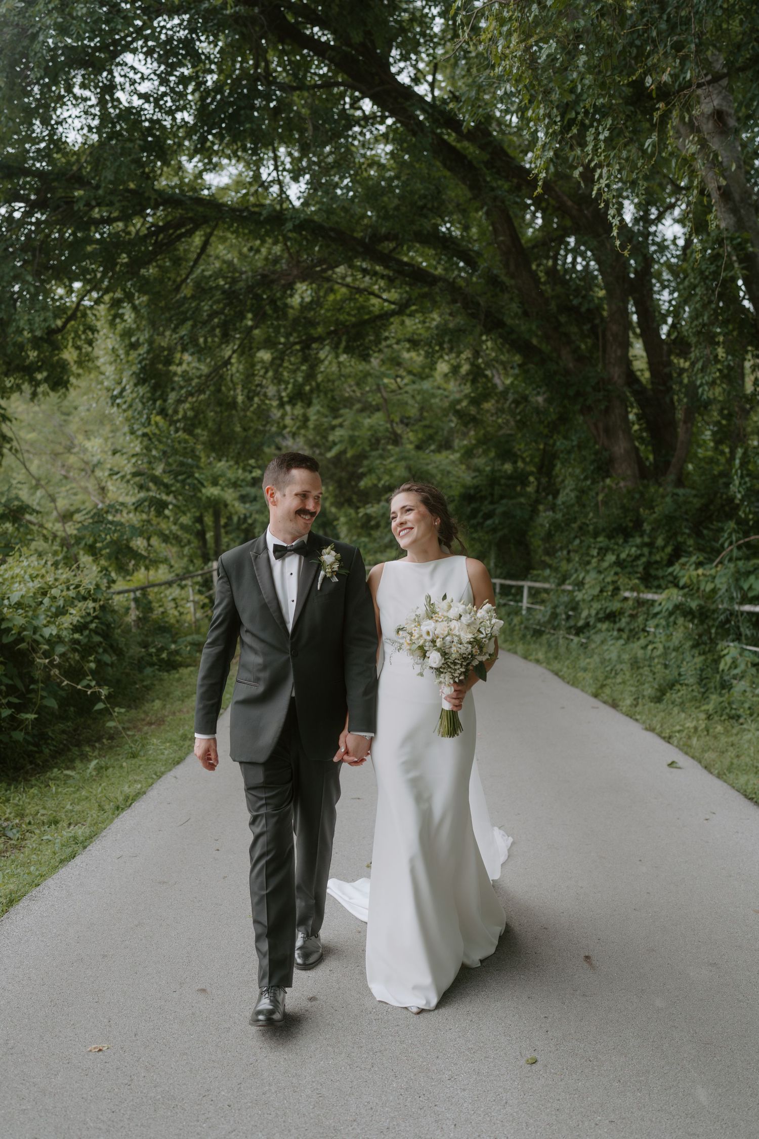 A couple shares a romantic moment while walking together on their wedding day along a peaceful path.
