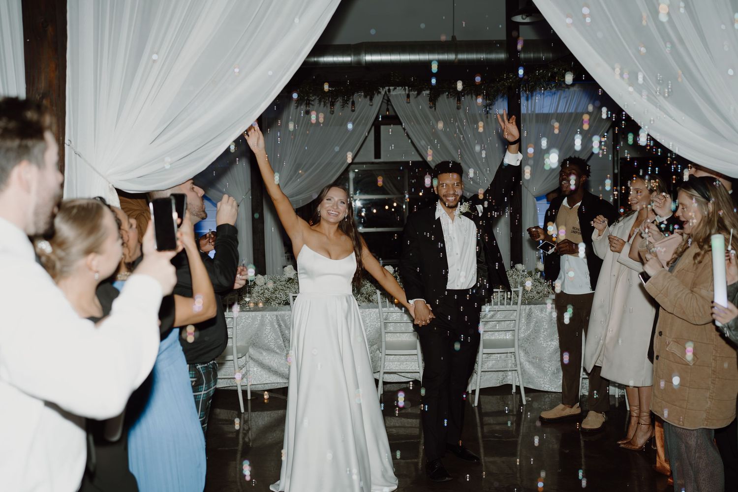 Wedding celebration with guests dancing under white draping and string lights.