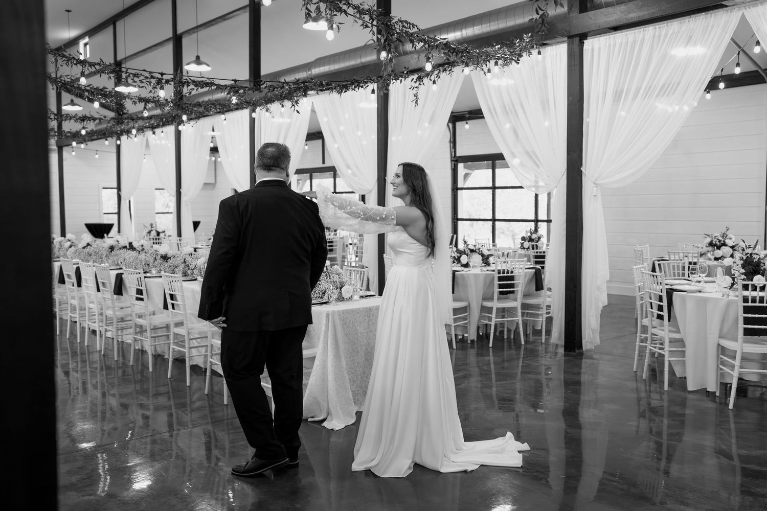 A black and white photo of a wedding reception venue with elegant table settings and string lights.