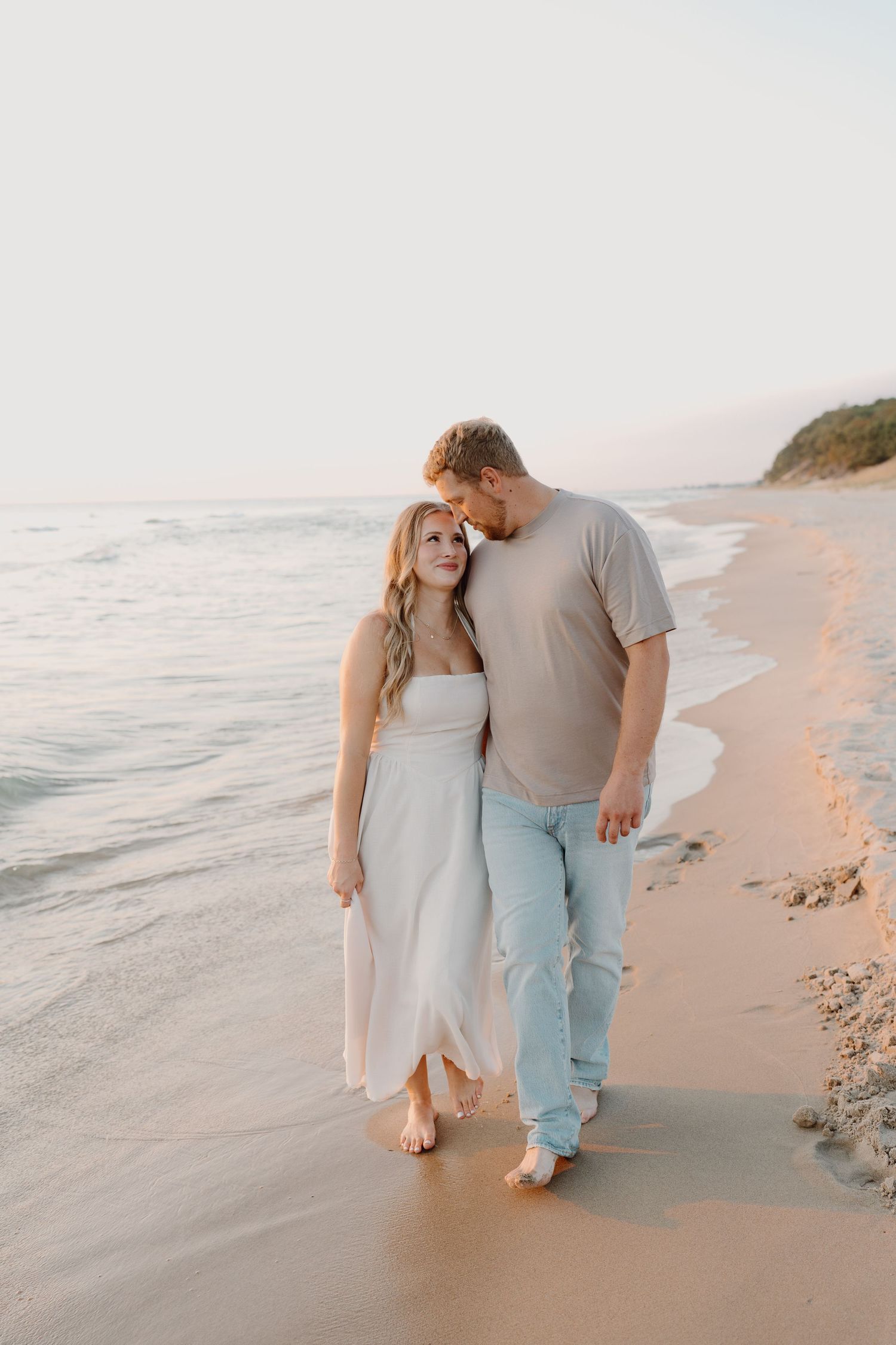 A romantic beach photoshoot captures a couple walking along the shoreline at dusk.