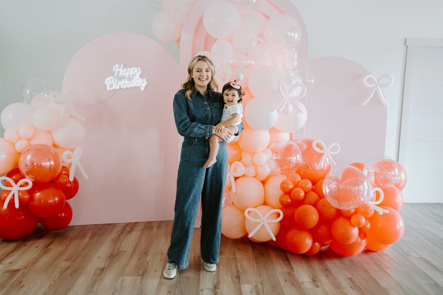 Birthday celebration setup featuring gradient coral balloon installation and wooden floors.