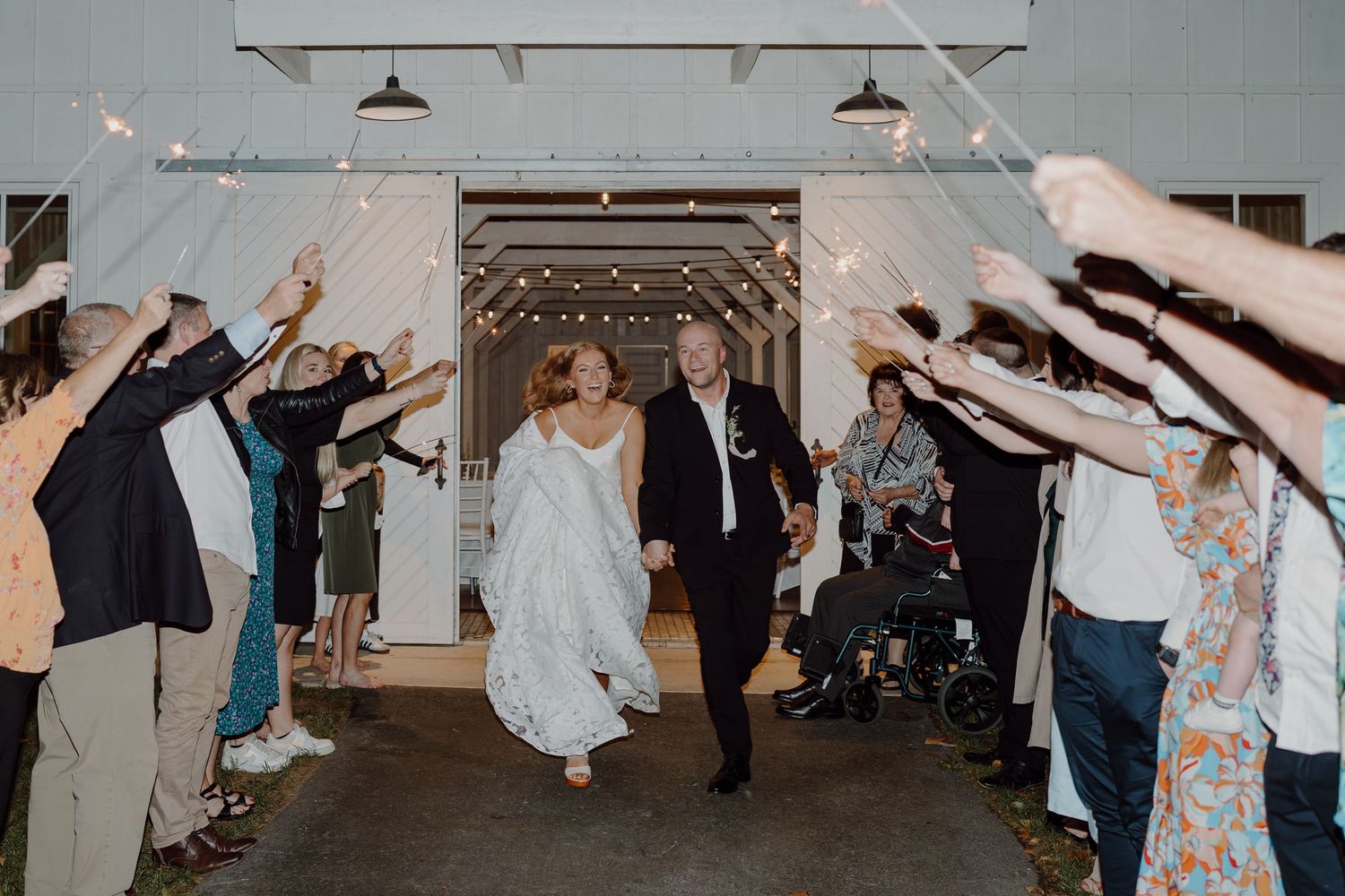 Wedding guests line a tunnel holding sparklers as couple walks through.