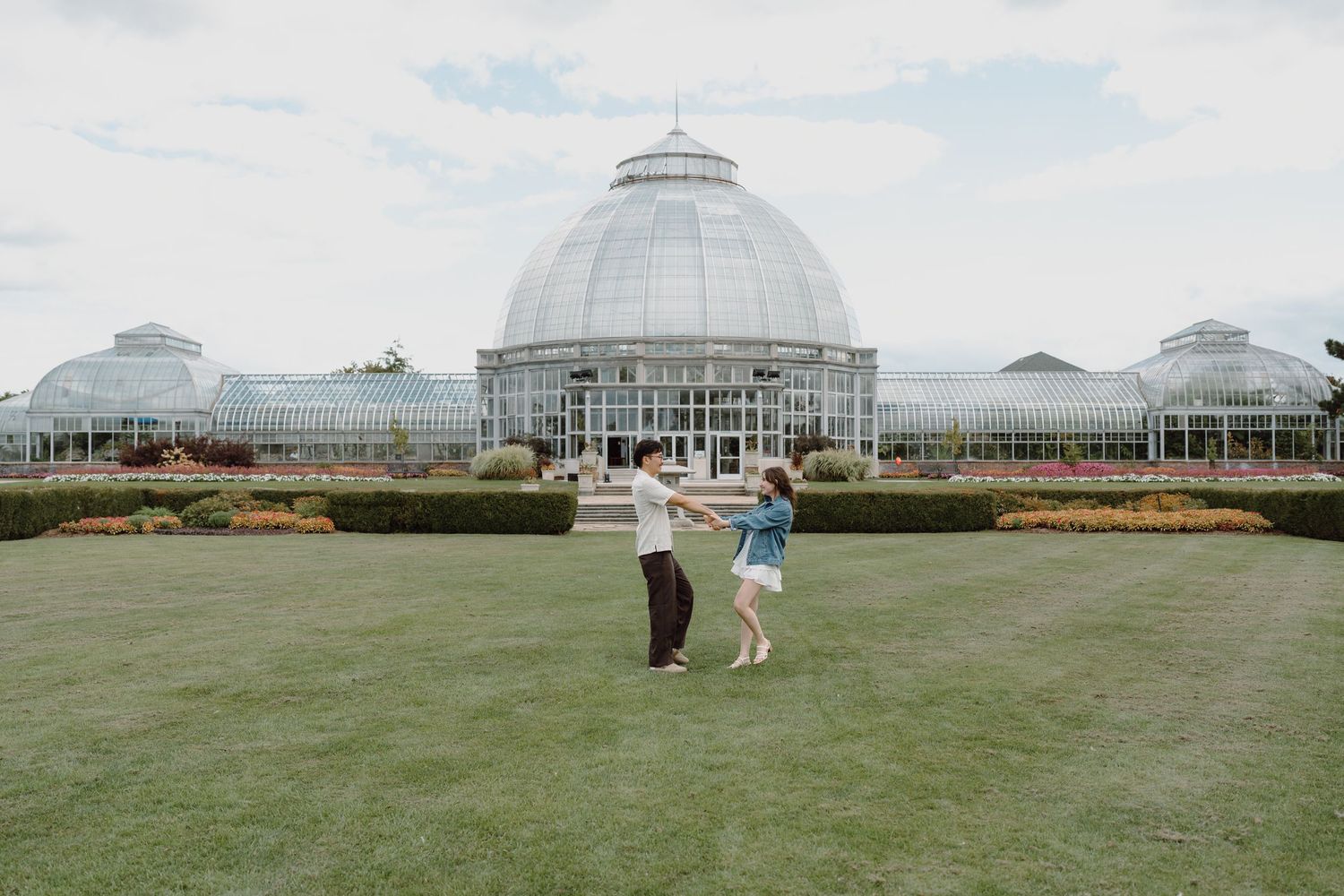 Wide panoramic view of a glass conservatory building with people on the expansive front lawn.