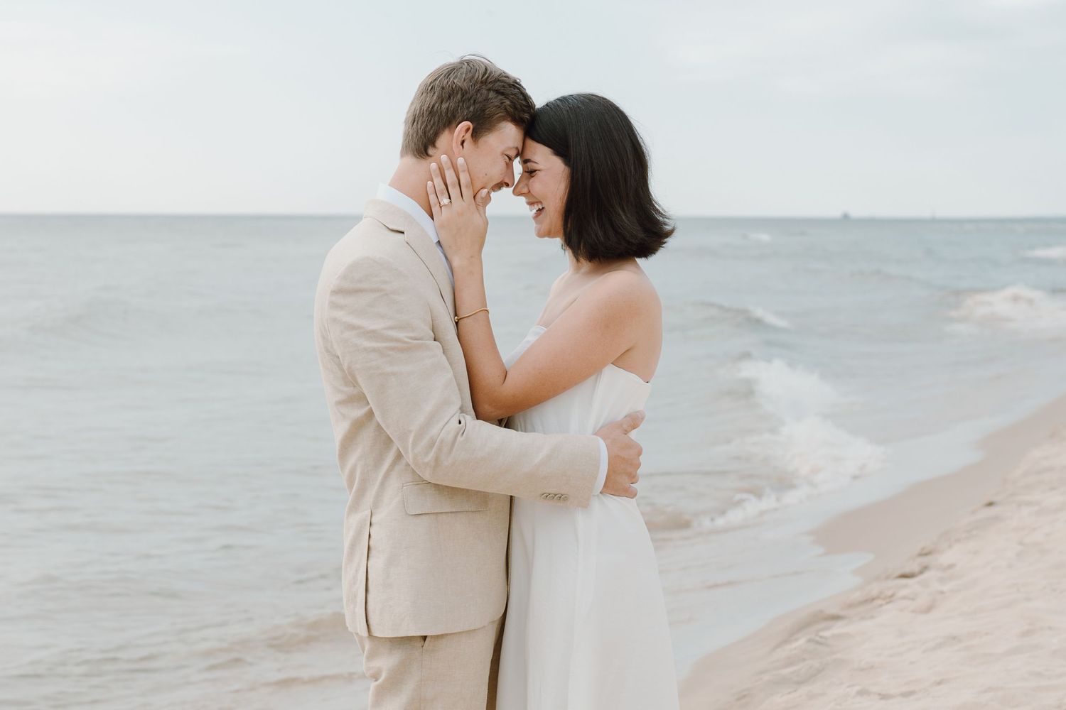 A couple in wedding attire shares an intimate moment against a serene beach backdrop.