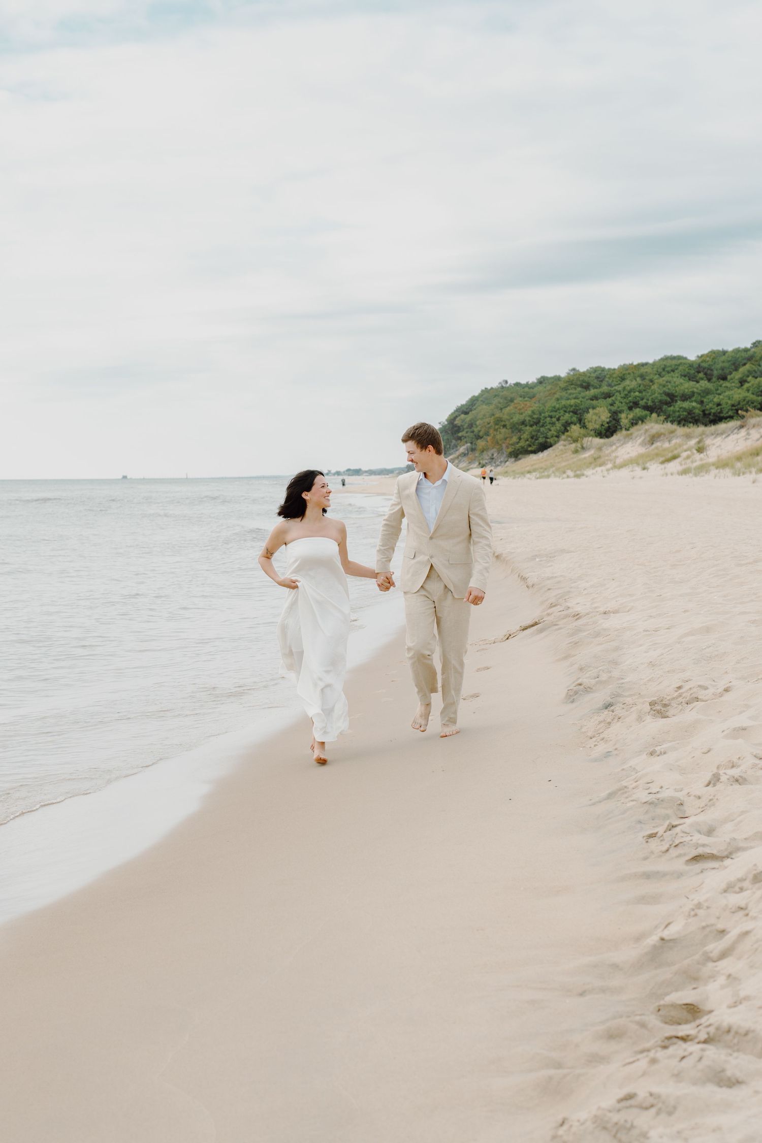 Couple in light-colored attire playfully running along the shoreline of a secluded beach.