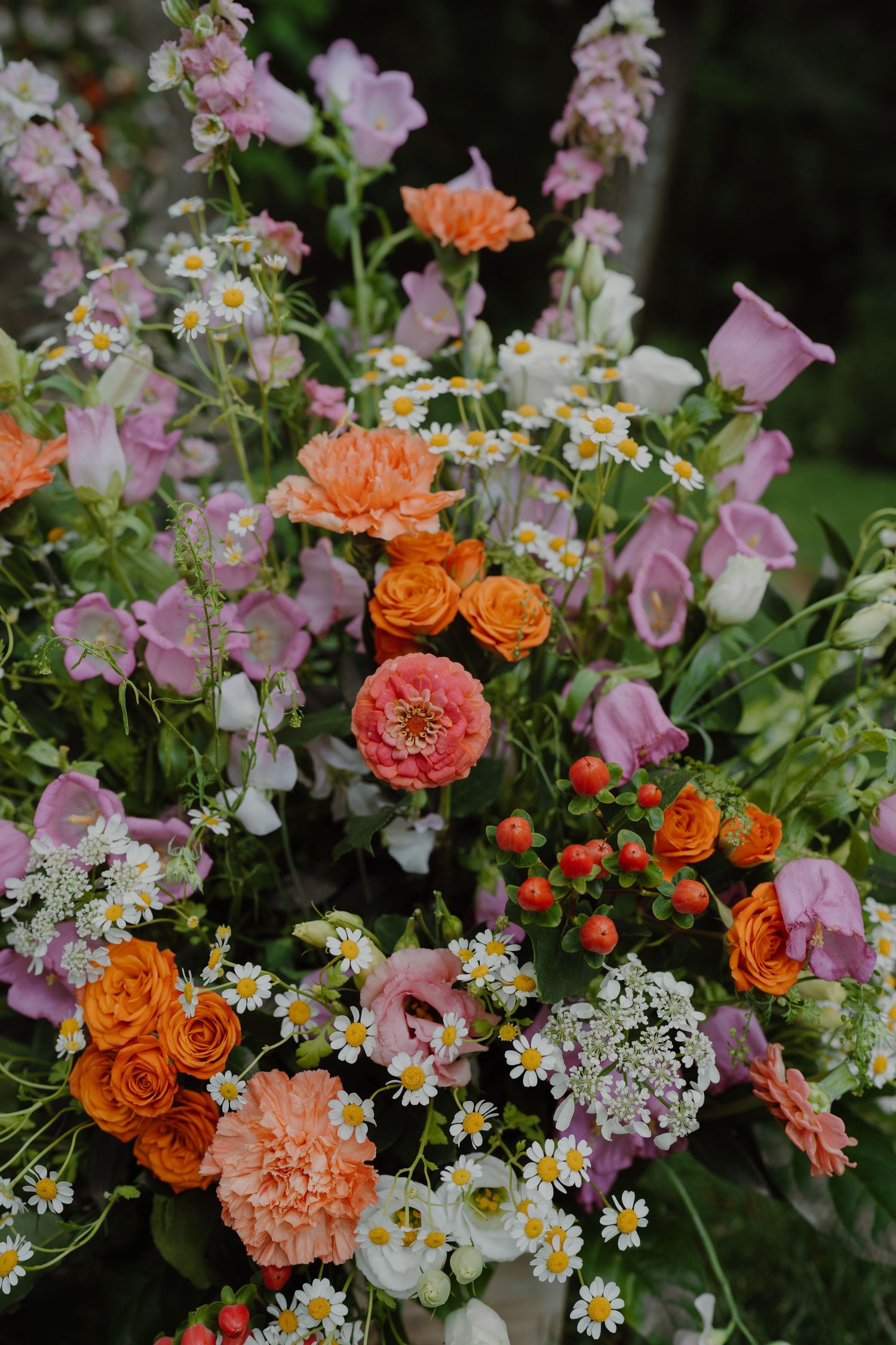 Vibrant floral arrangement featuring orange roses, pink carnations, white daisies, and delicate greenery.