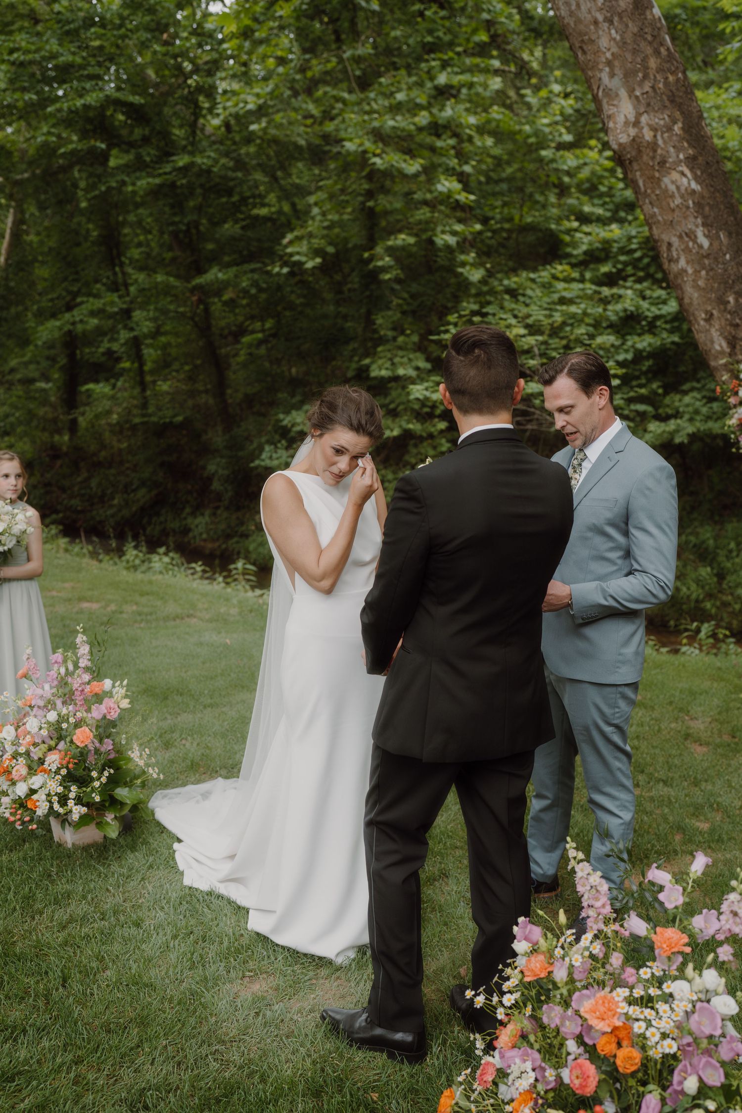 A touching wedding ceremony scene in a natural outdoor setting with pink and orange flower arrangements.