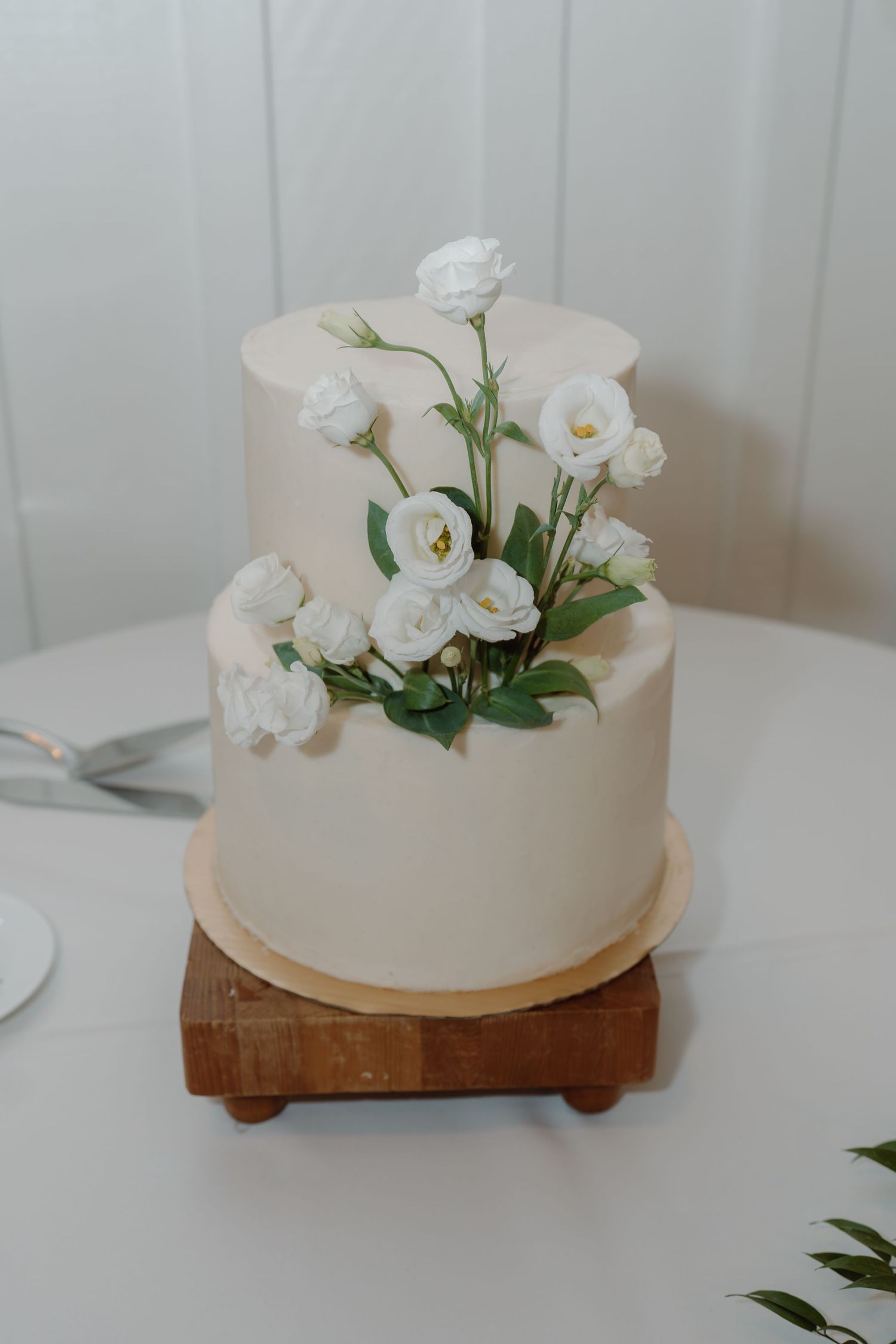 Elegant white wedding cake decorated with fresh white flowers on a wooden stand.