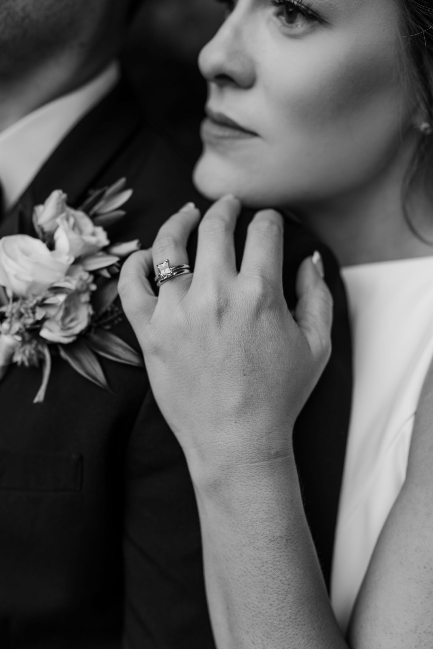 Close-up black and white photo of an engagement ring and floral bouquet detail.