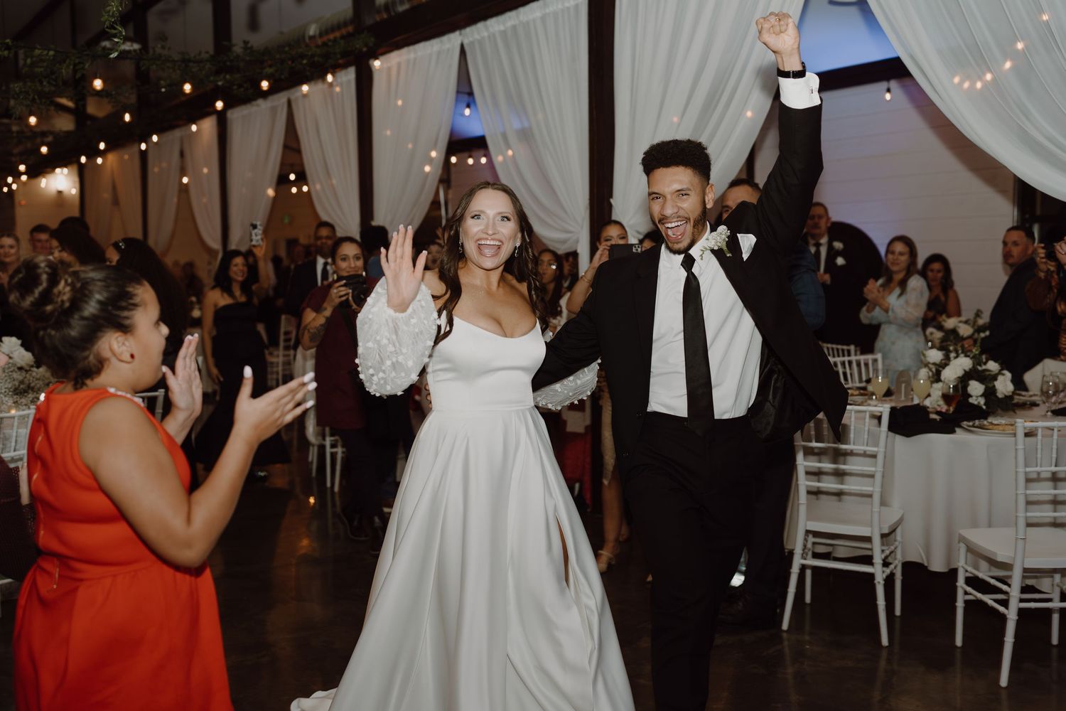 Wedding celebration with couple making entrance at indoor reception venue with string lights.