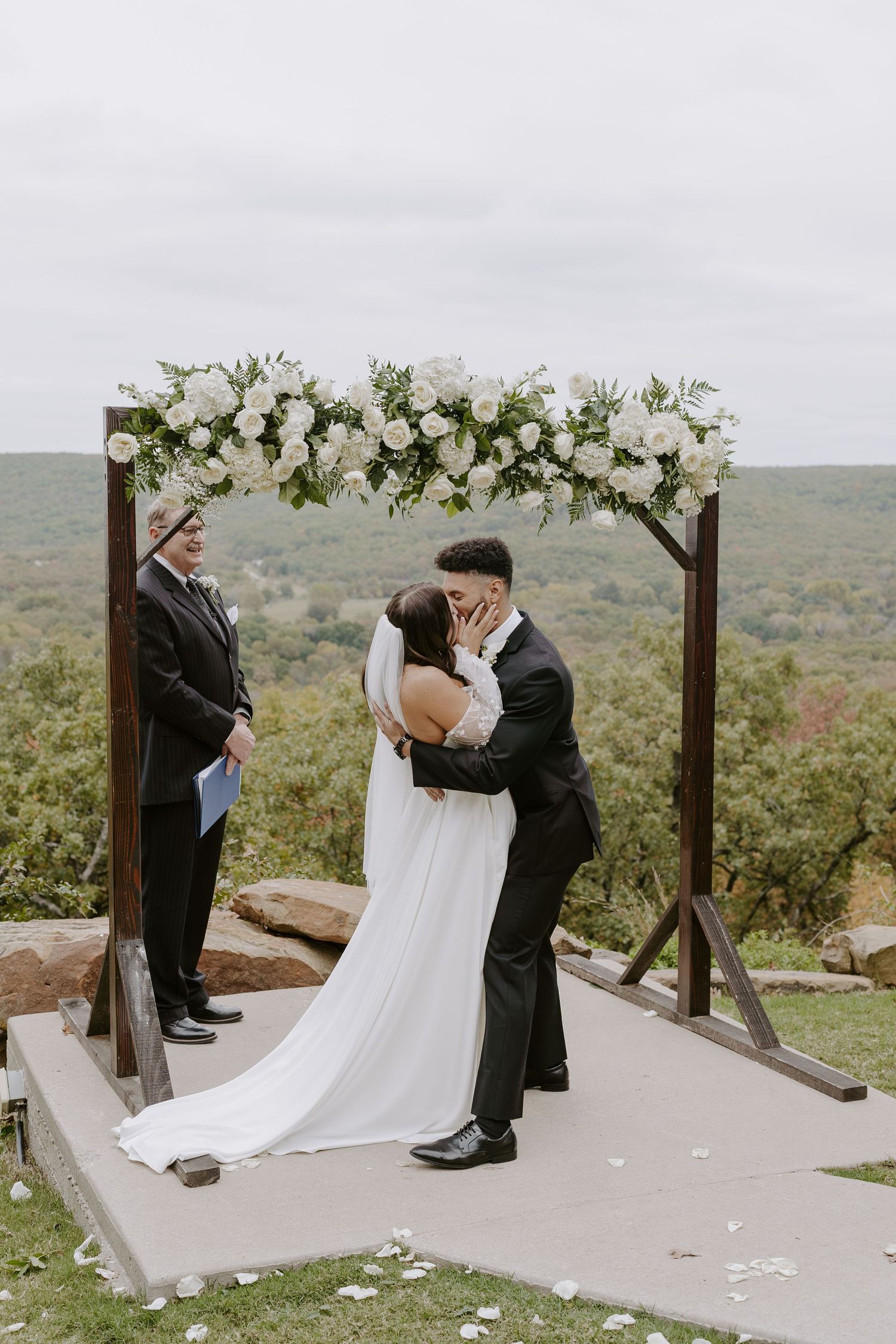 Intimate wedding ceremony moment under floral arch with scenic mountain backdrop.