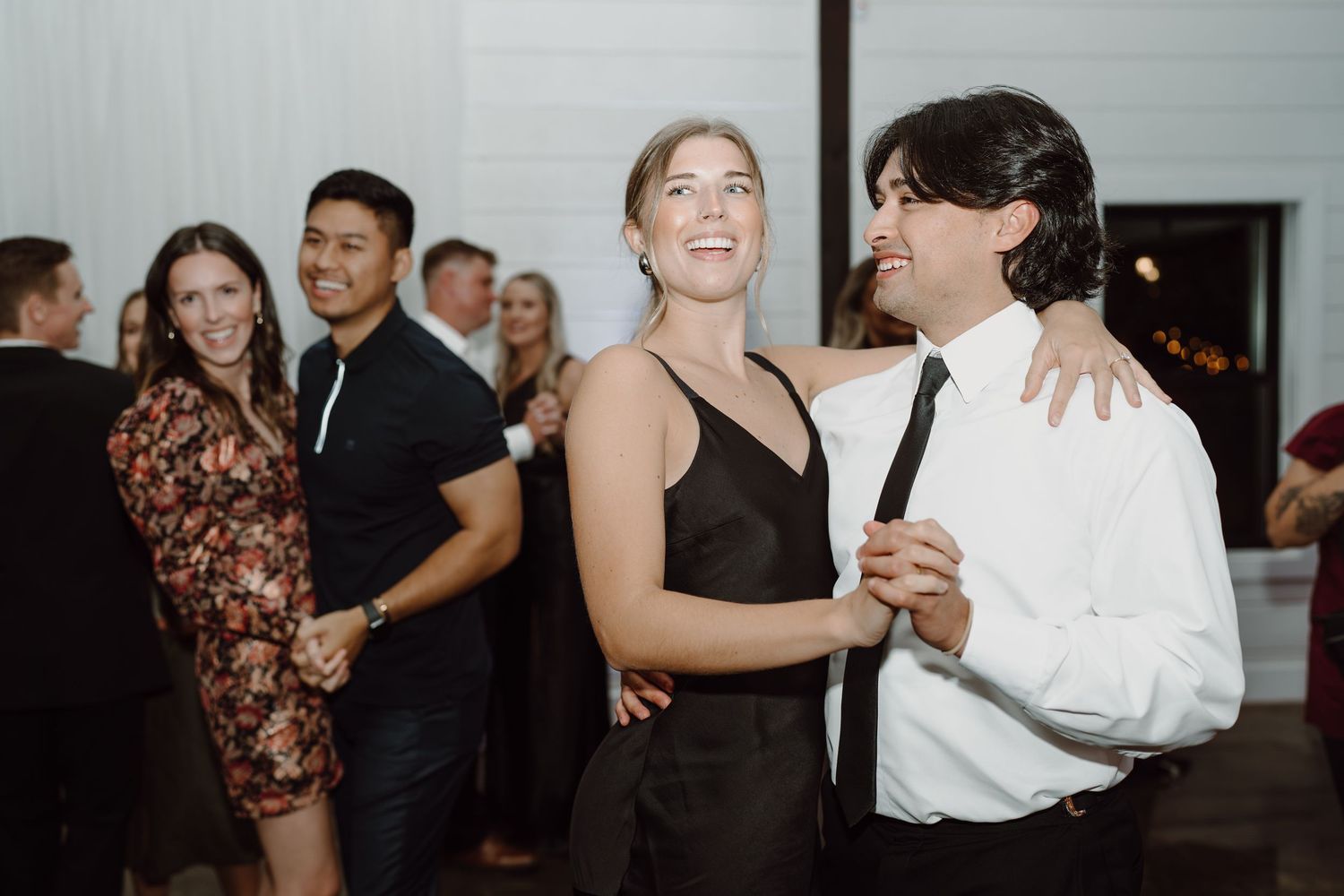 Couples dancing together at an elegant wedding reception with white walls and festive atmosphere.