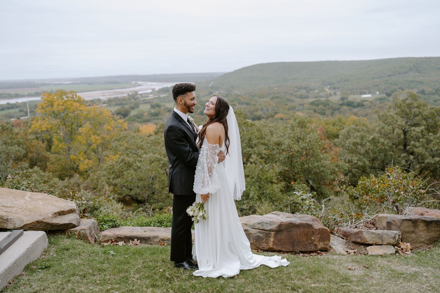 A couple shares an intimate moment on a scenic hilltop overlooking rolling landscapes during their wedding day.