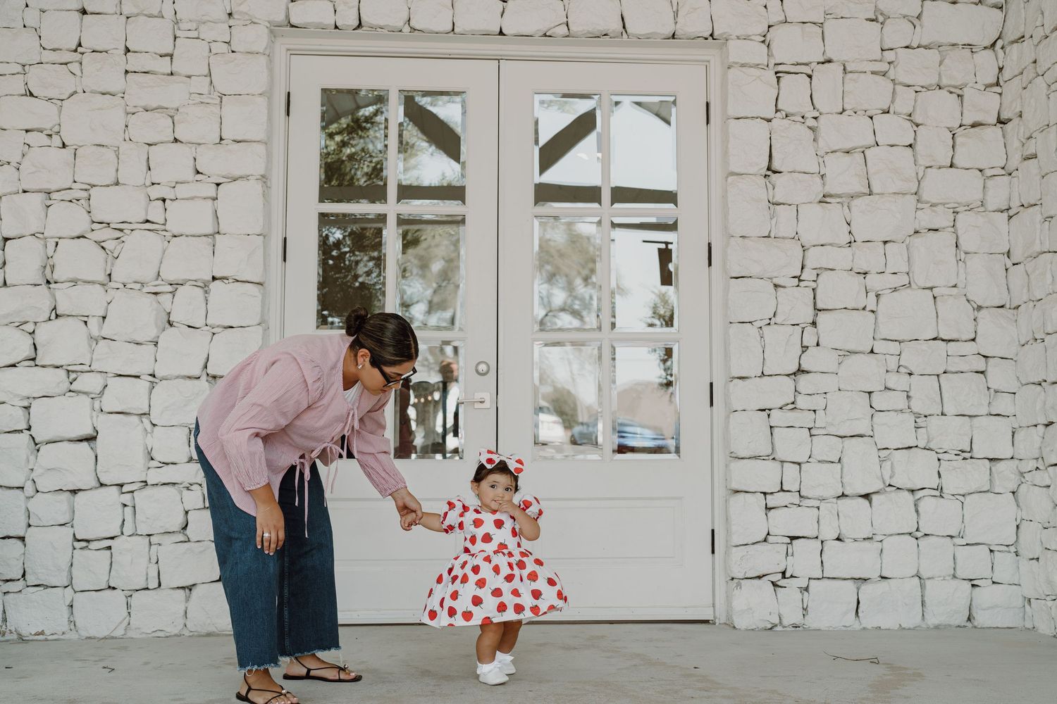 Parent and small child in heart-print dress playing by stone building.