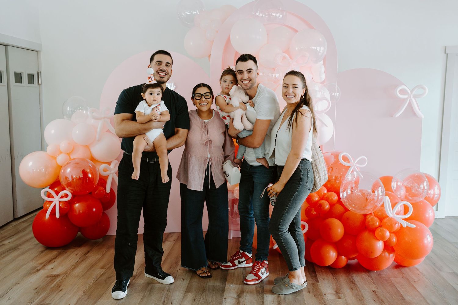 Family gathering in front of an elegant balloon installation with pink and orange hues.