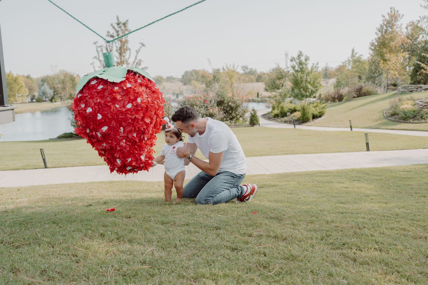 A red heart-shaped decoration swings through the air on a grassy hill near a lake.