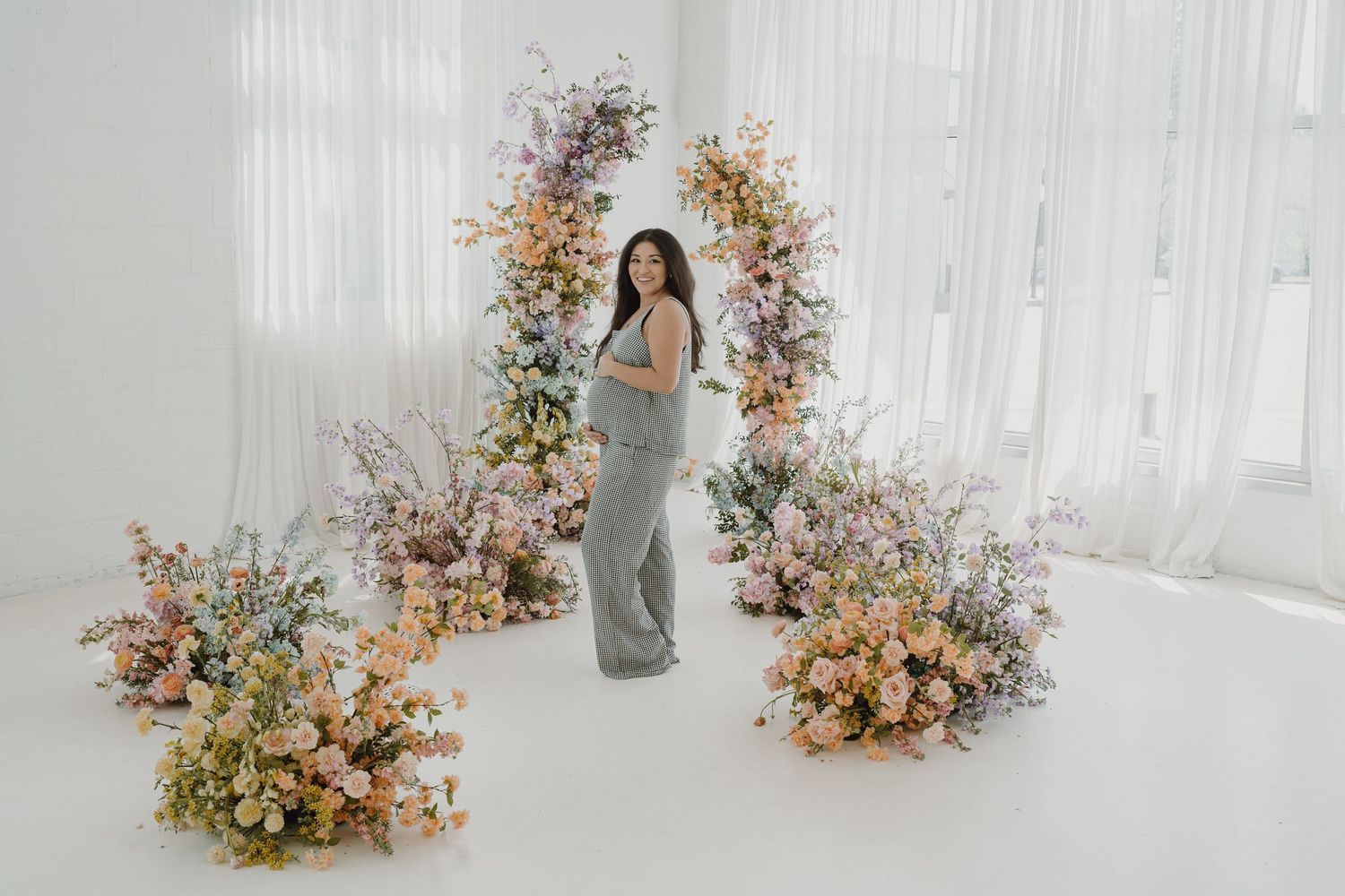 Dreamy maternity photo with colorful floral arrangements in light-filled studio space.