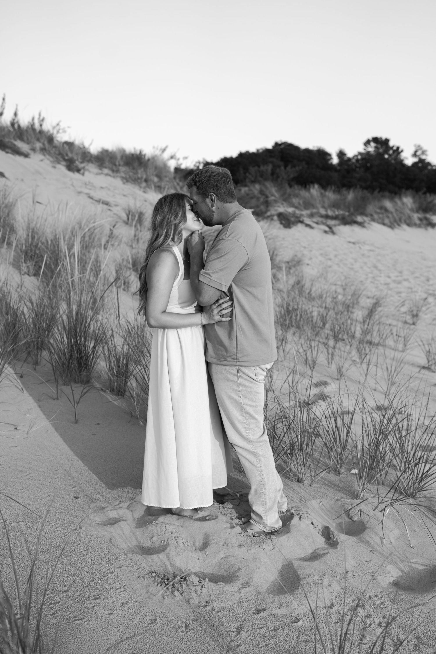 A romantic moment between a couple standing in the beach dunes at sunset.