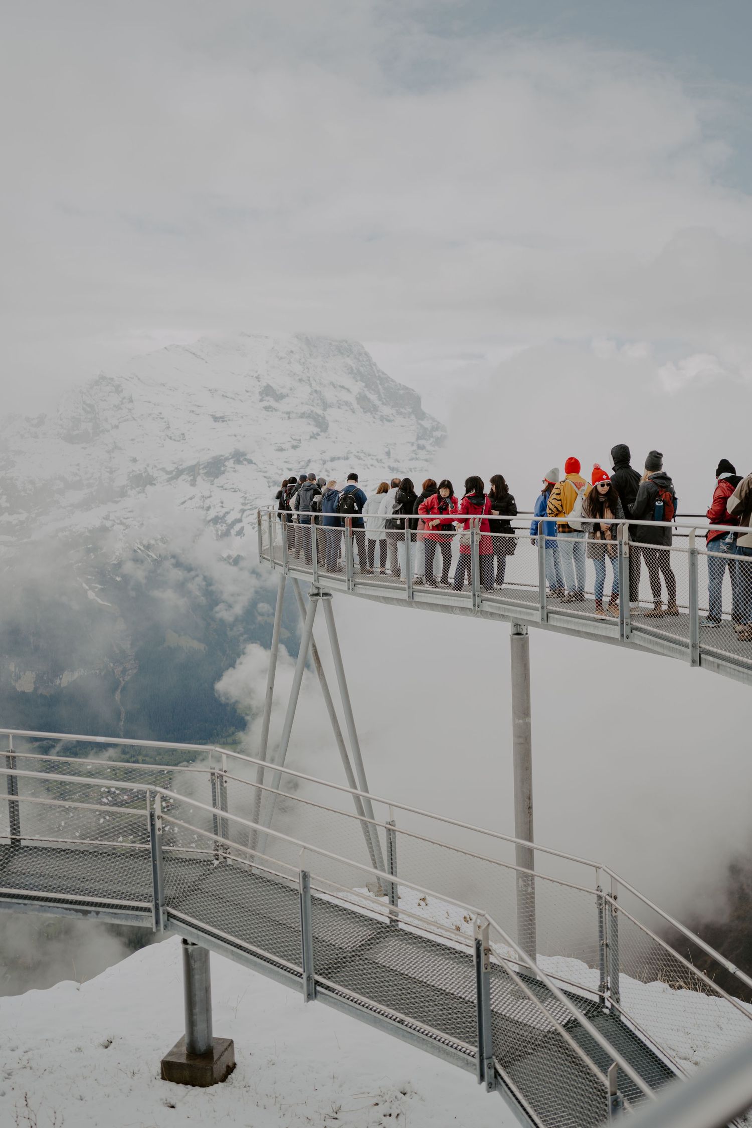 Observation deck filled with tourists overlooking snow-covered mountain peaks.