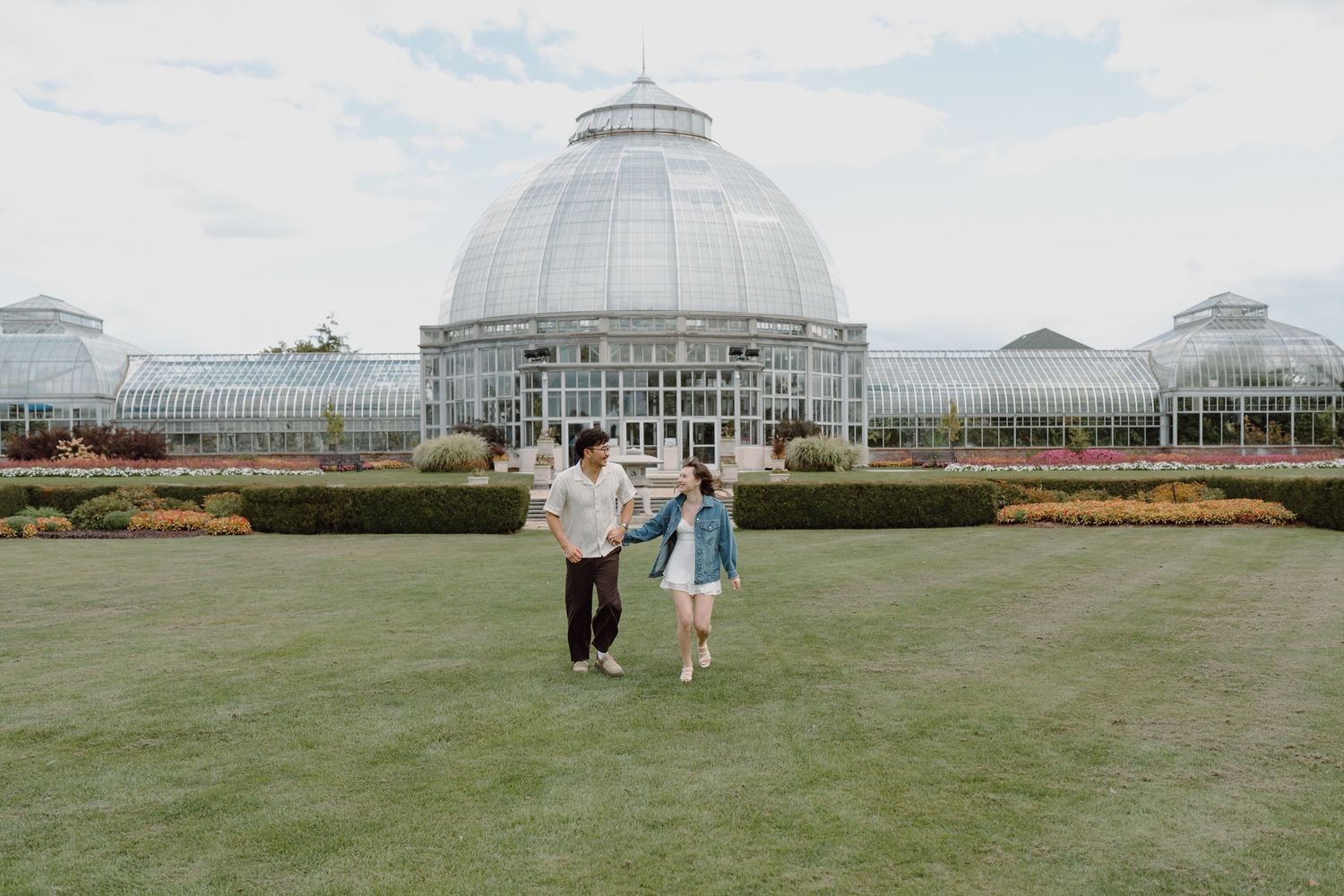Scenic view of a glass-domed botanical garden with people enjoying the outdoor lawn space.