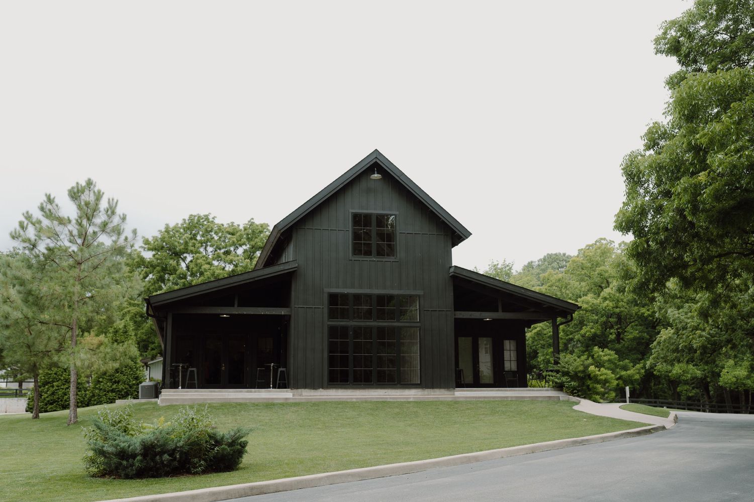 Modern black barn structure with large windows set against a green rural landscape.