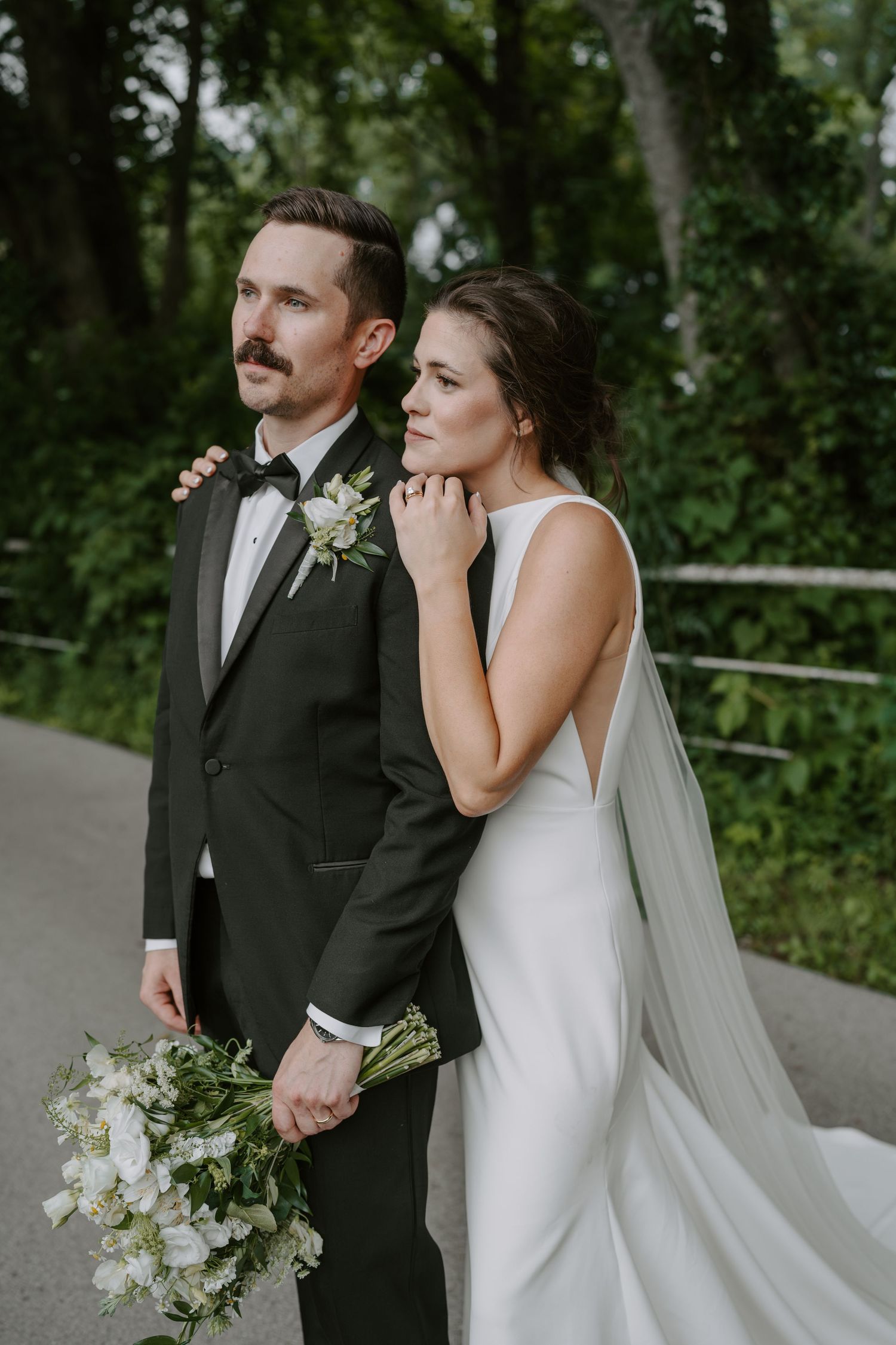 Elegant wedding portrait featuring a classic white gown and black tuxedo against a forest backdrop.