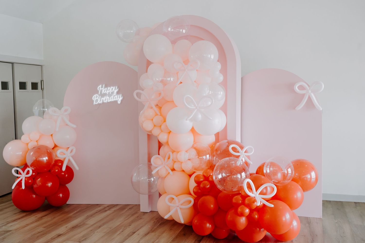 Elegant balloon arch installation in shades of pink and red with white decorative elements.