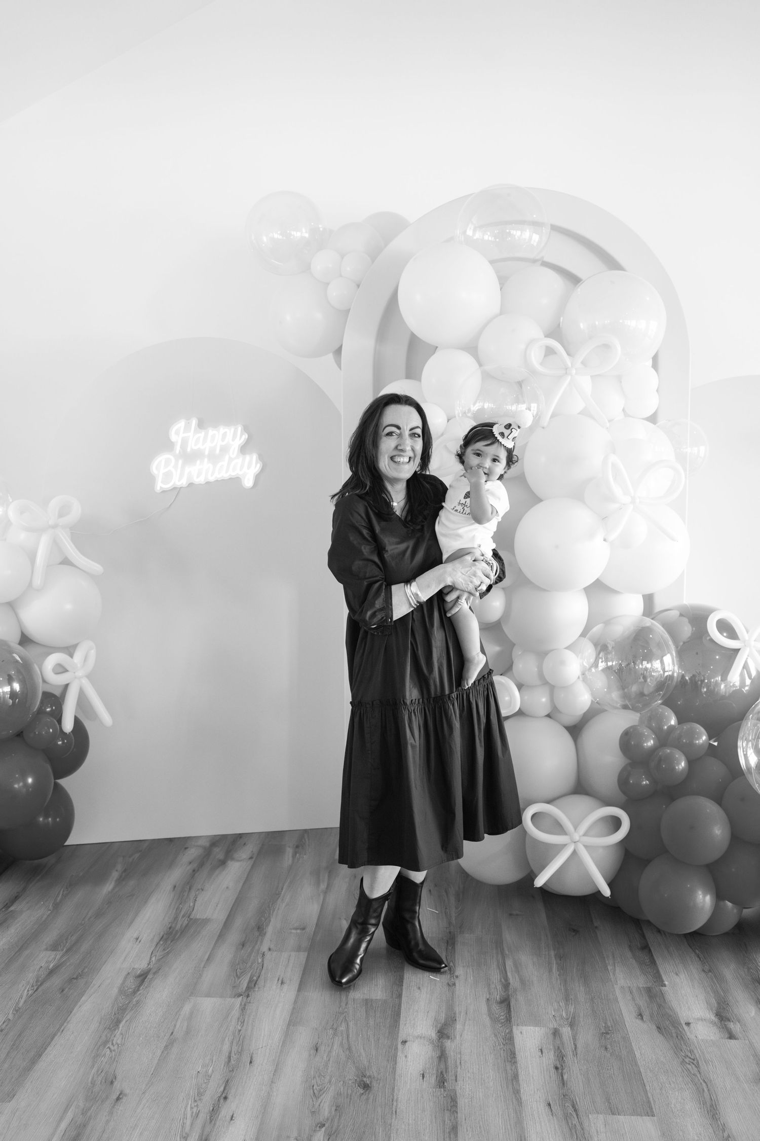 Black and white photo of birthday celebration setup with balloon garland and wooden flooring.
