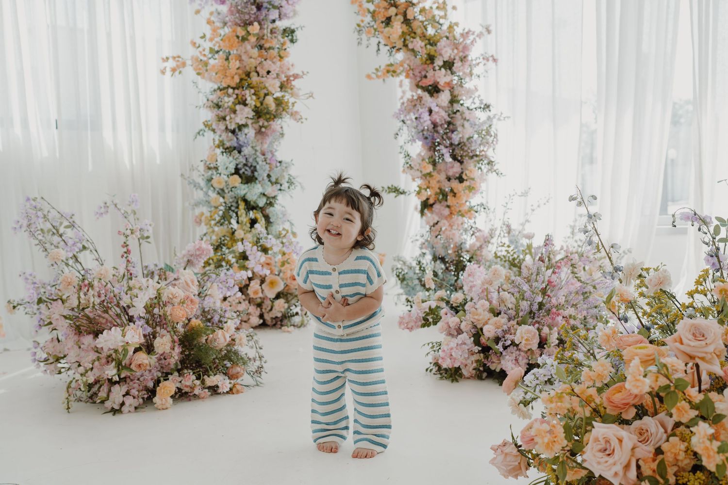 A whimsical photo setup with striped outfit and floral decorations in a white studio space.