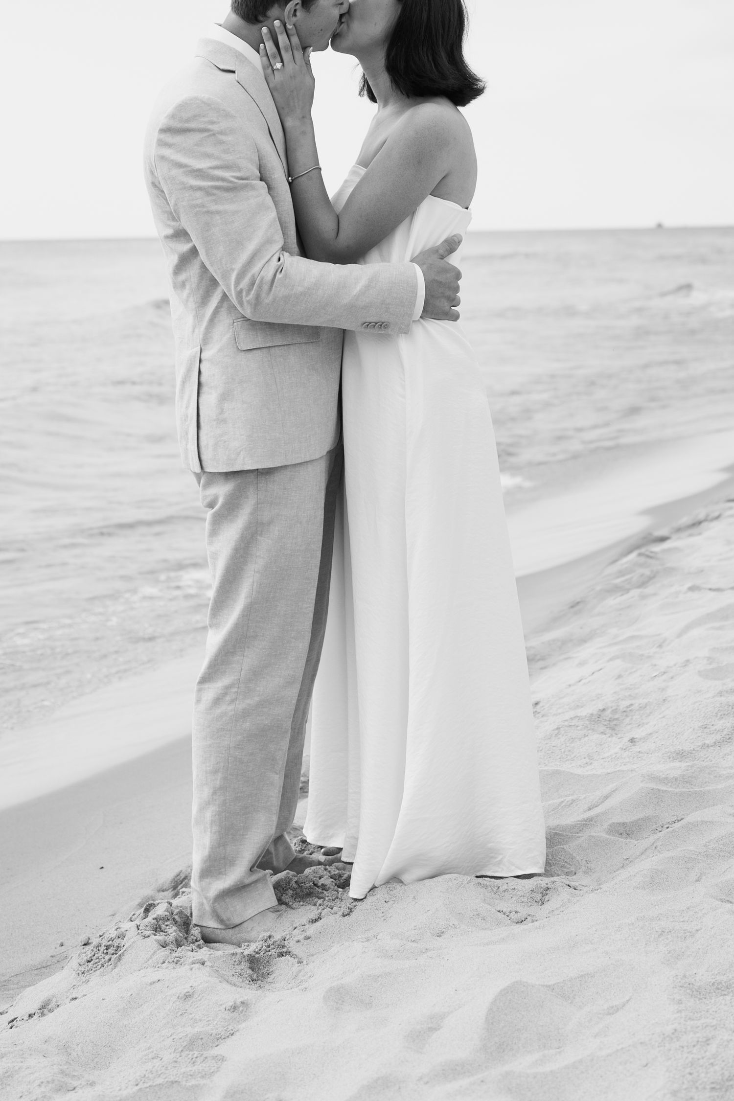 A couple shares an intimate moment on the beach in black and white.