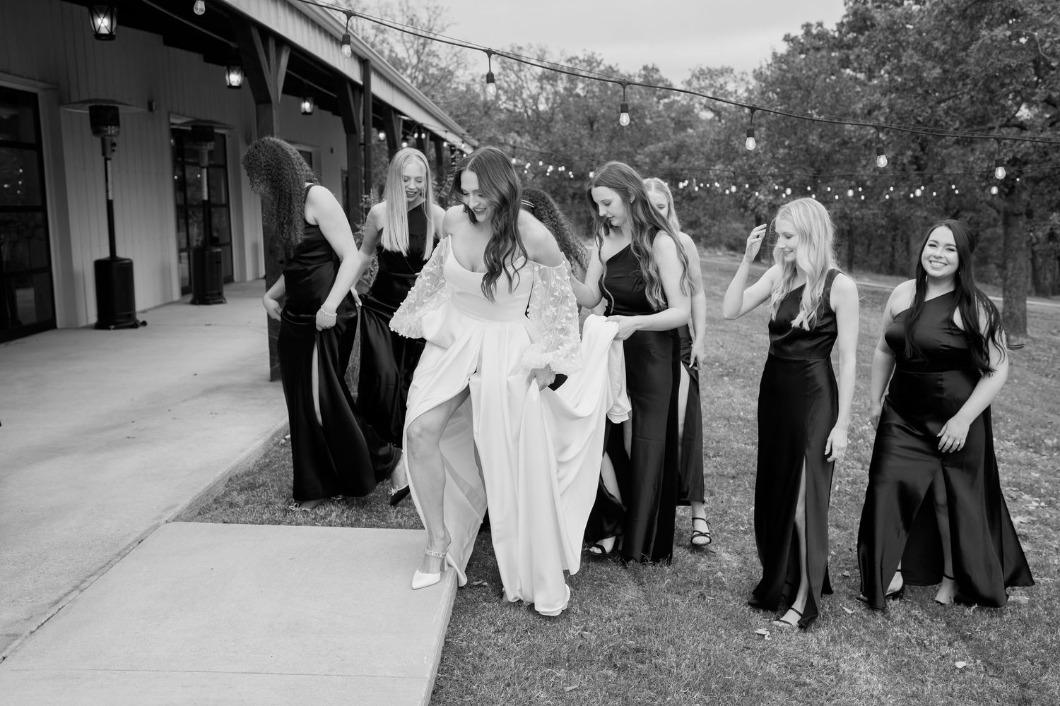 Black and white photo of wedding party celebrating with joyful gestures outside venue.