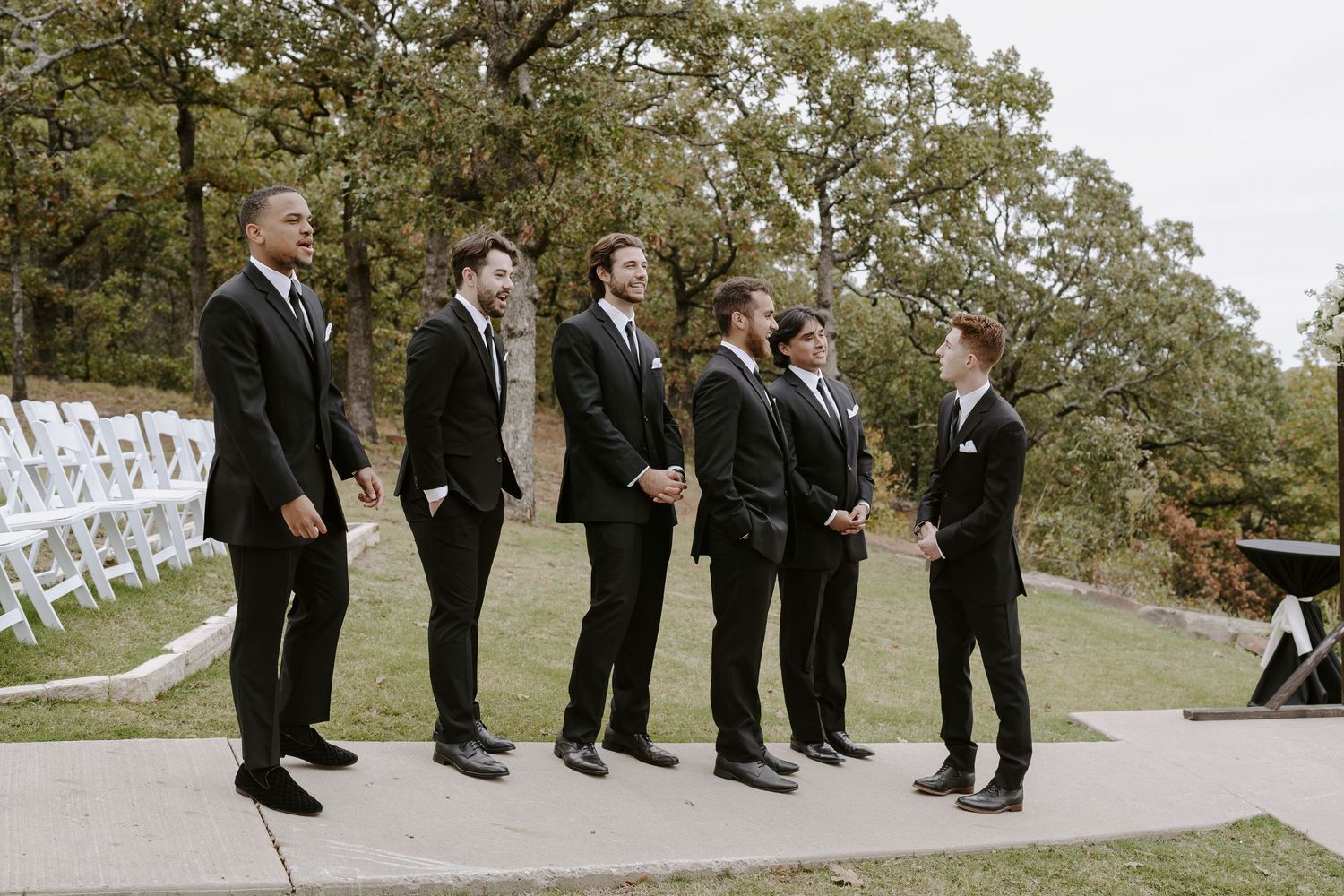 Groomsmen arranged in casual poses along rustic outdoor walkway.